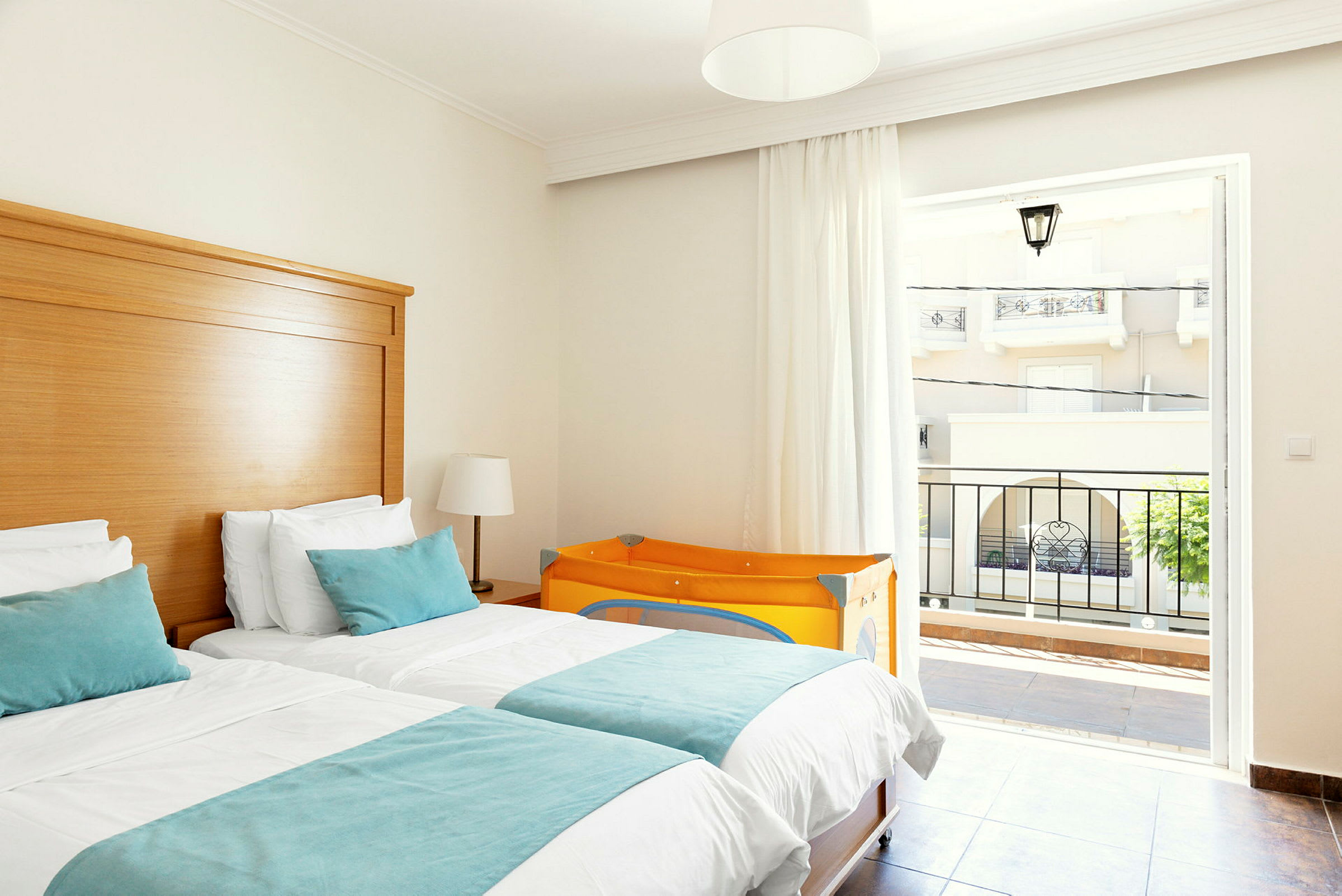 Hotellrum med två enkelsängar, ljusa möbler och en orange barnsäng. (AI-genererad text)