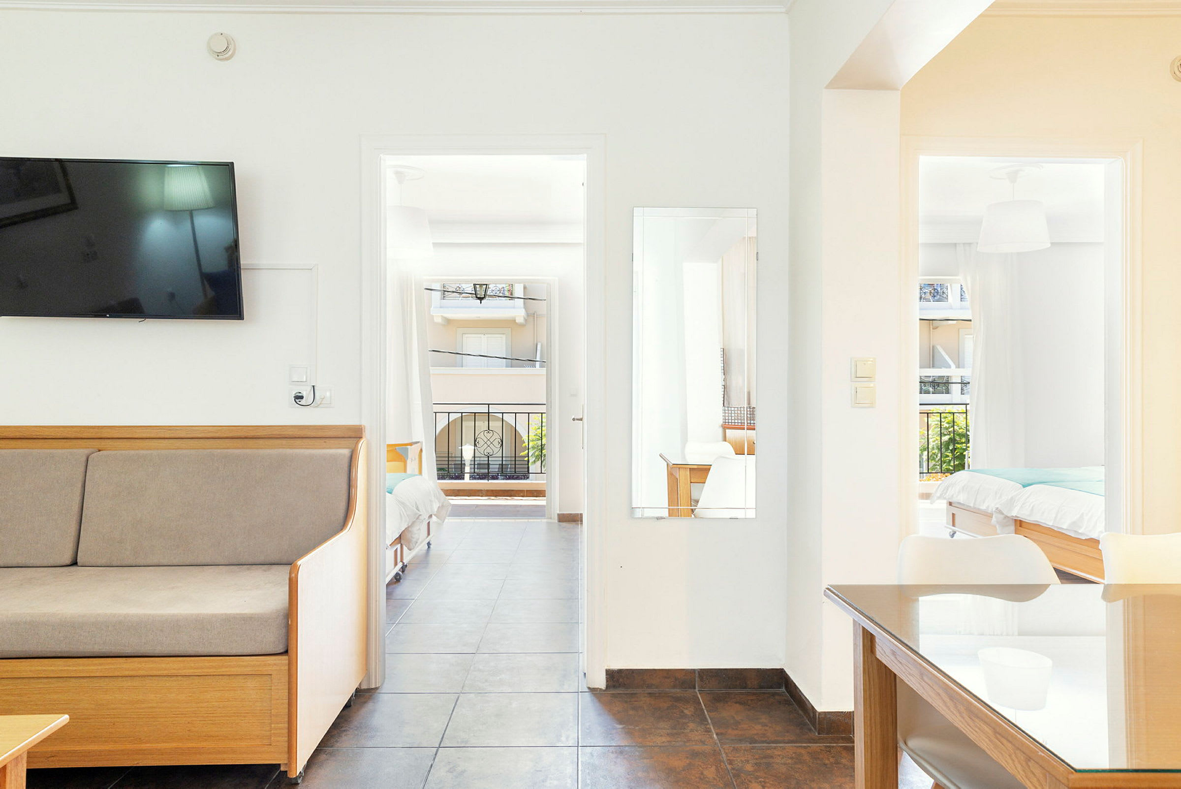 Ett ljust hotellrum med en soffa, TV, bord och två sängar. Rummet har en balkong. (AI-genererad text)