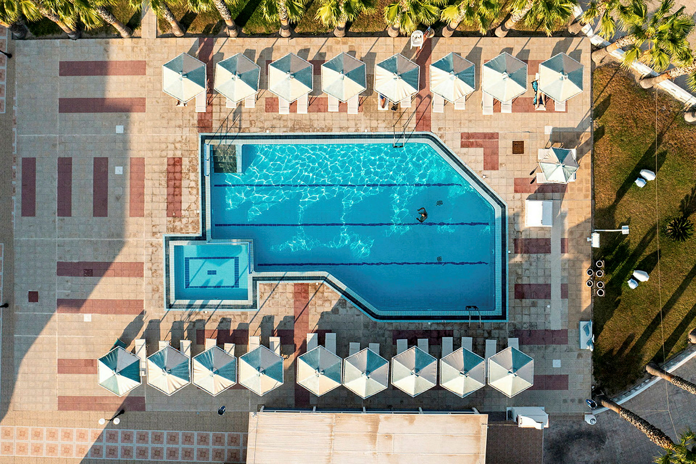 En överblicksbild av en pool med parasoller och solstolar runtom. (AI-genererad text)