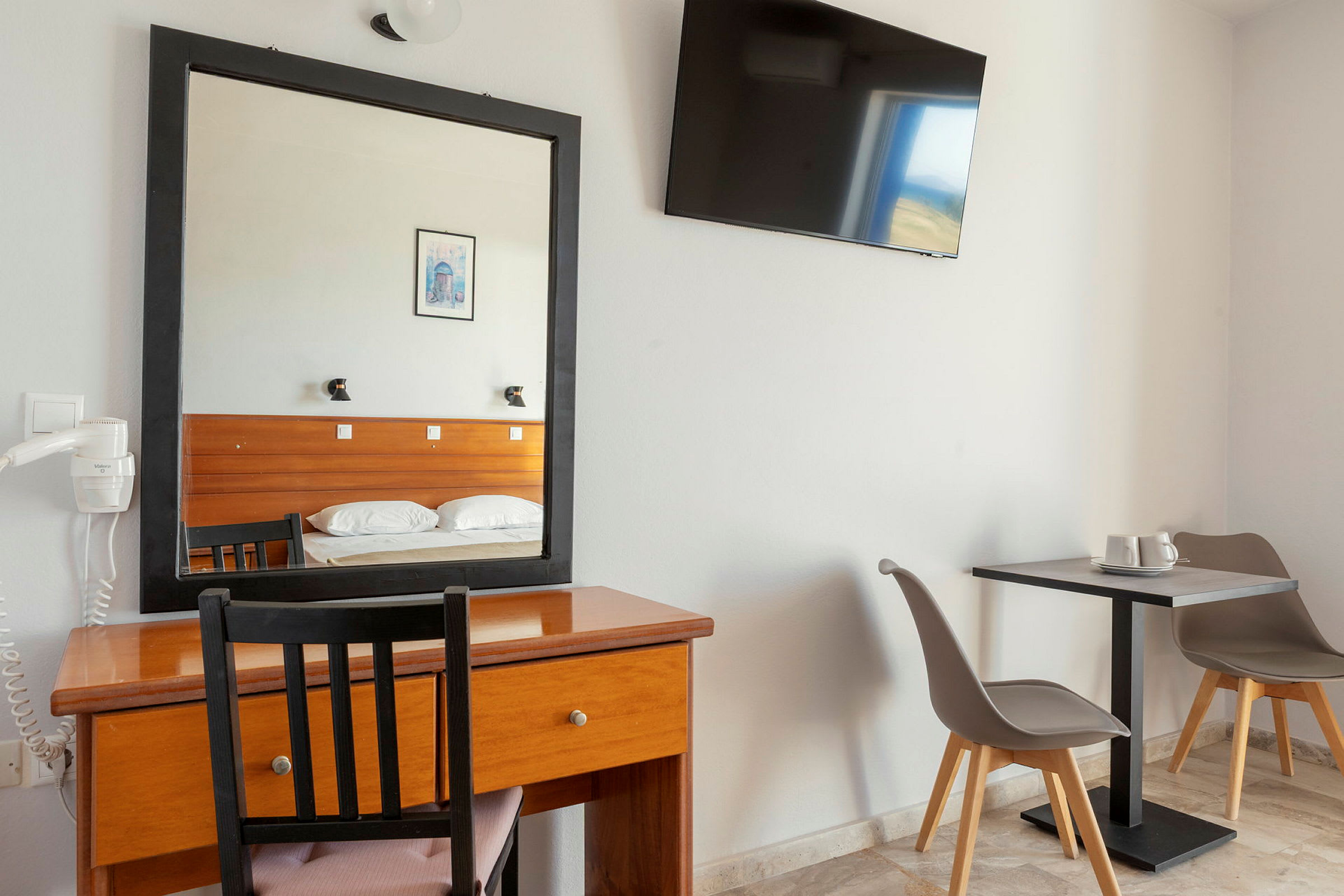 Hotellrum med skrivbord, spegel och TV på väggen. Till höger två stolar vid ett bord. (AI-genererad text)
