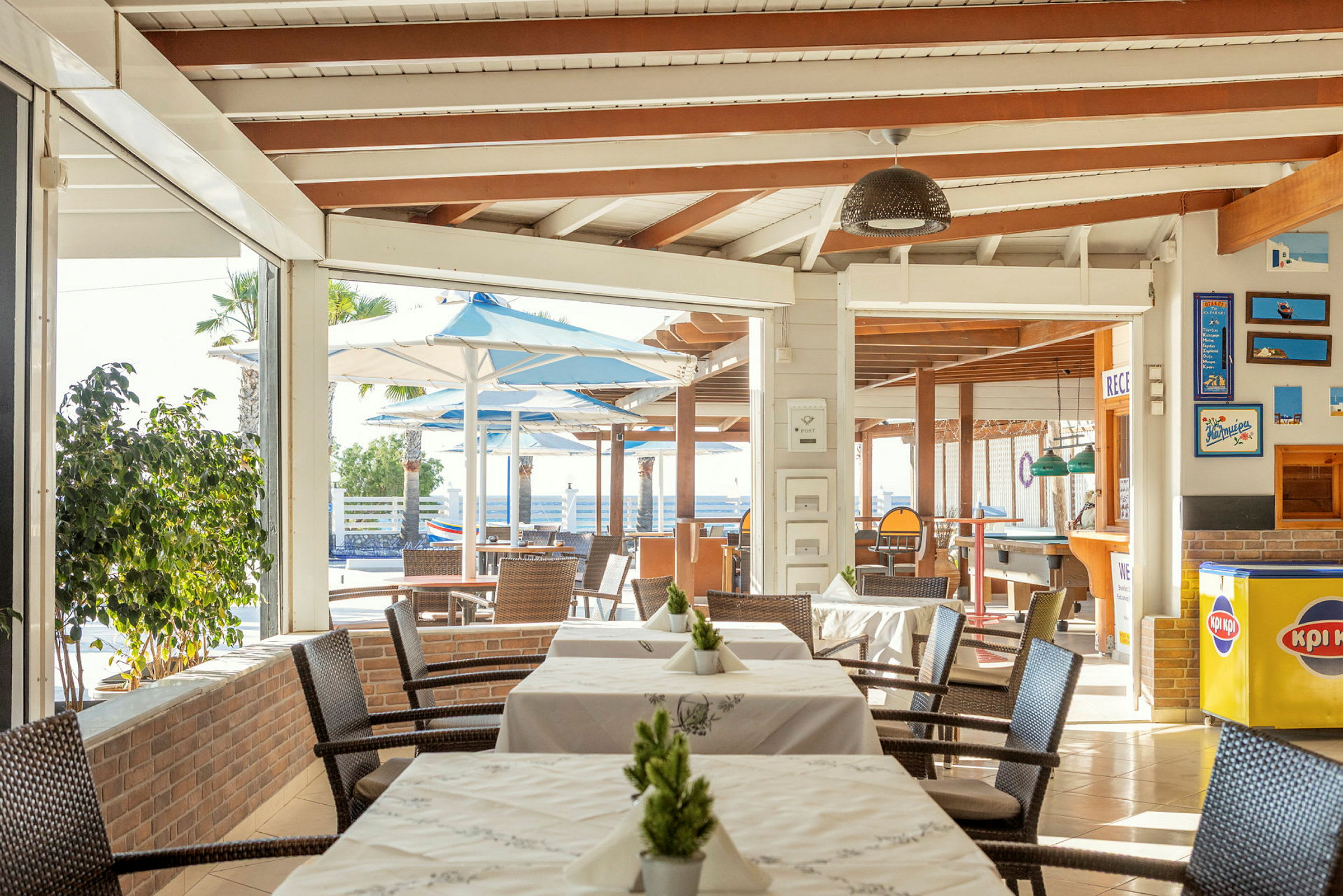 Restaurang med bord och stolar, utomhusområde med parasoller syns i bakgrunden. (AI-genererad text)