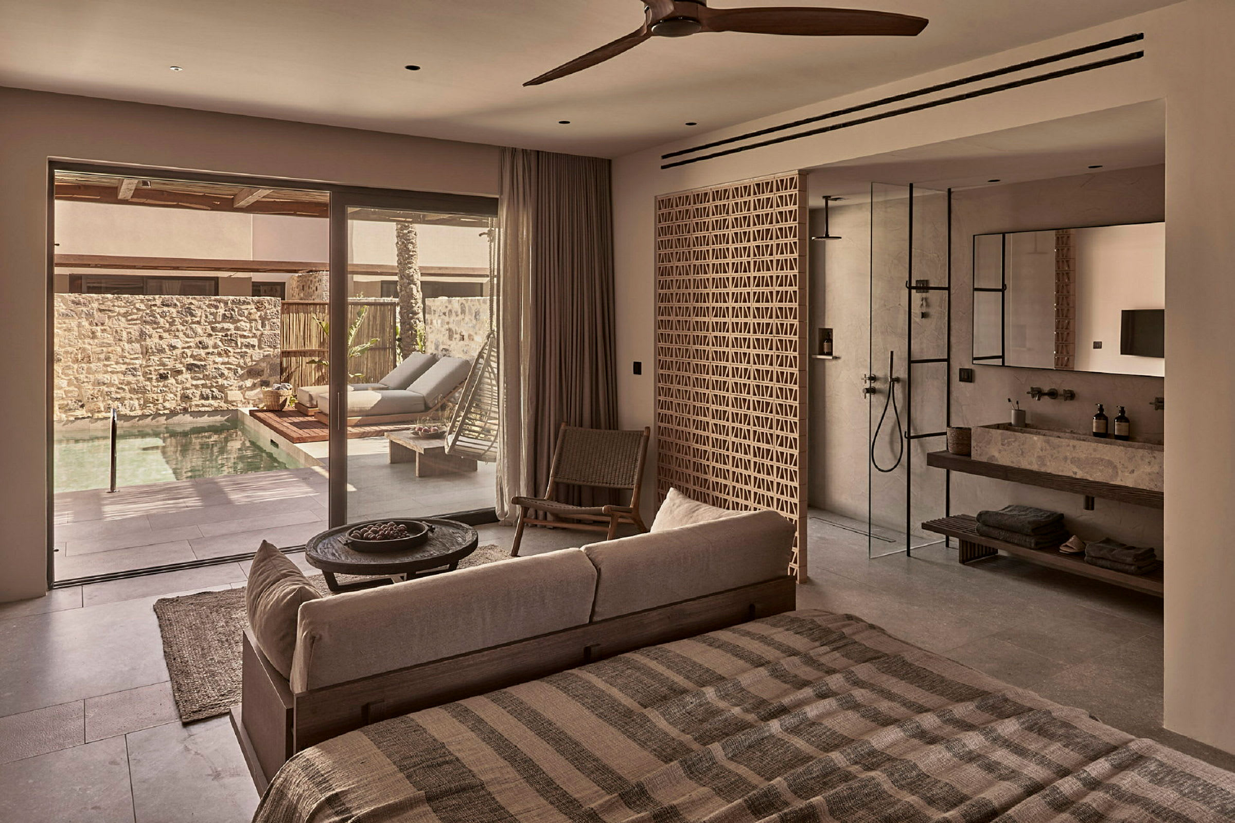 Interiör av ett modernt hotellrum med säng, sittgrupp och badrum, utsikt mot en privat pool genom glasdörrar. (AI-genererad text)