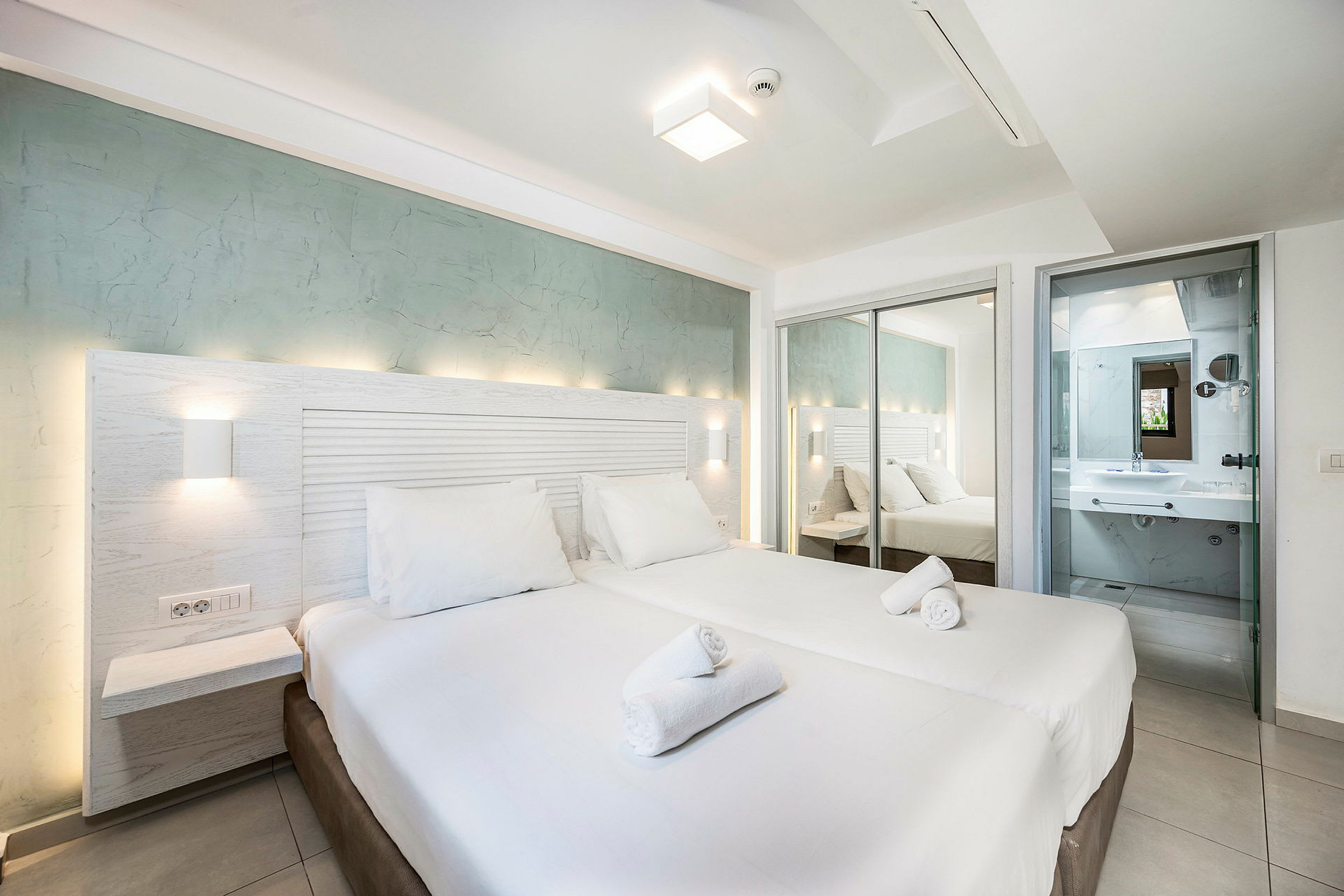 Ett hotellrum med en dubbelsäng, vit sängkläder, och badrum synligt i bakgrunden. (AI-genererad text)