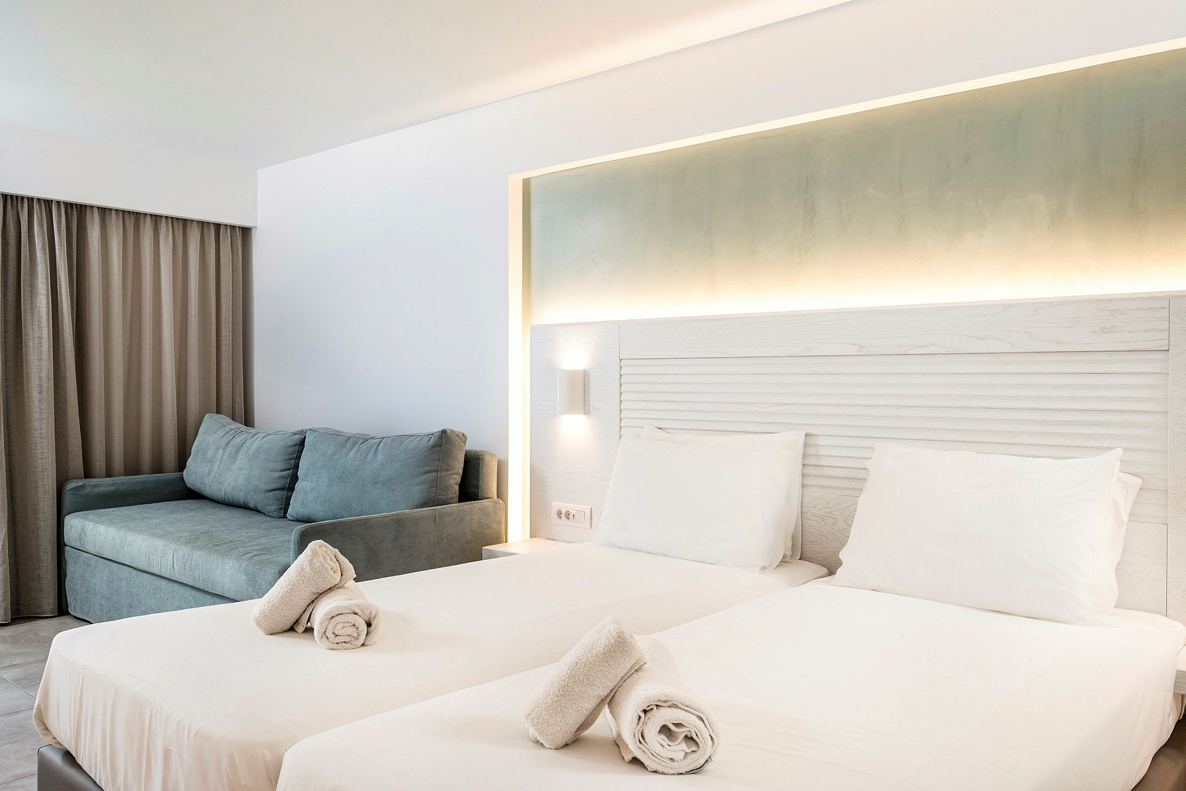Hotellrum med två enkelsängar, upplyst sänggavel och en soffa. (AI-genererad text)