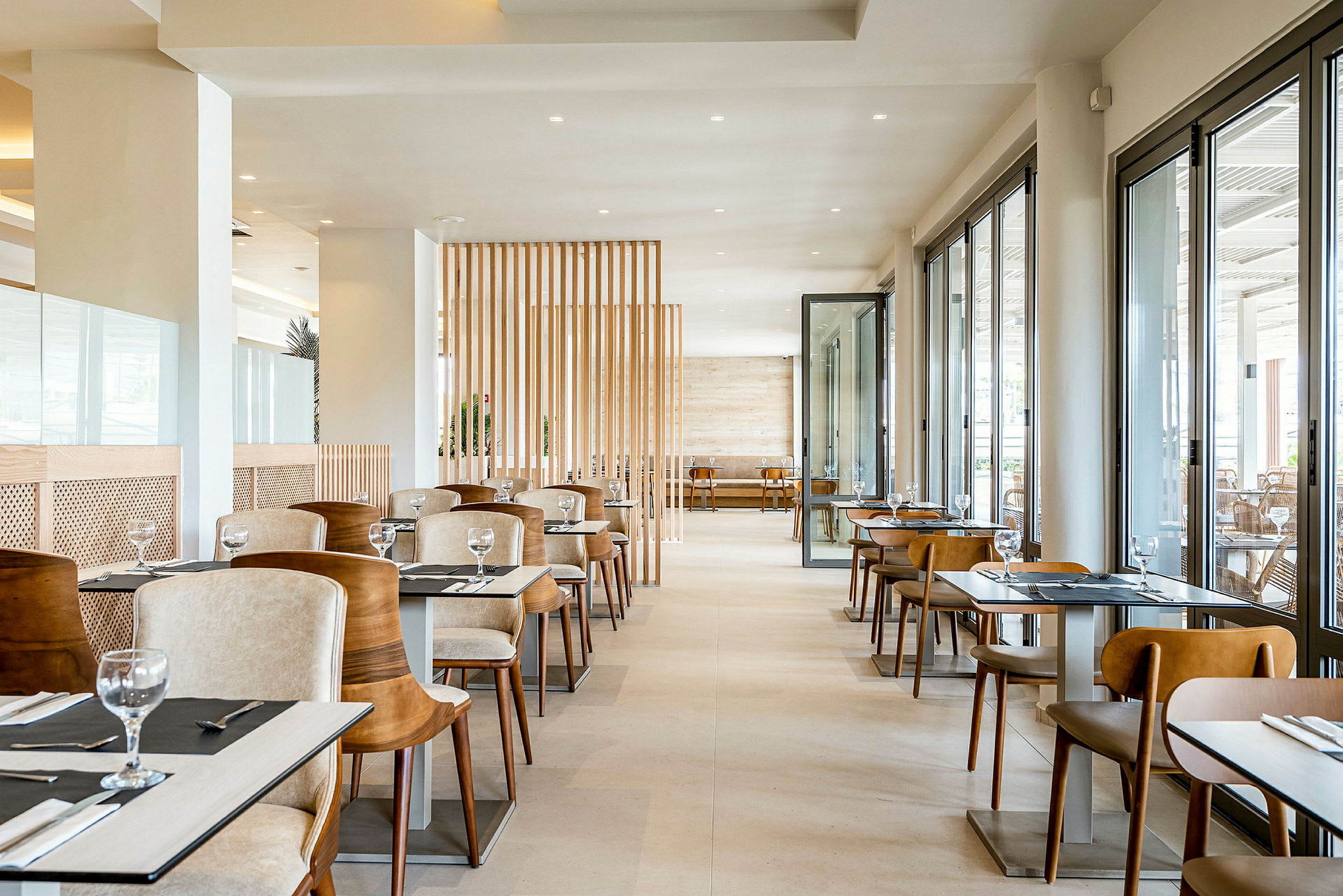 Restauranginteriör med bord och stolar. Ytan är ljus och modern med stora fönster som släpper in dagsljus. (AI-genererad text)