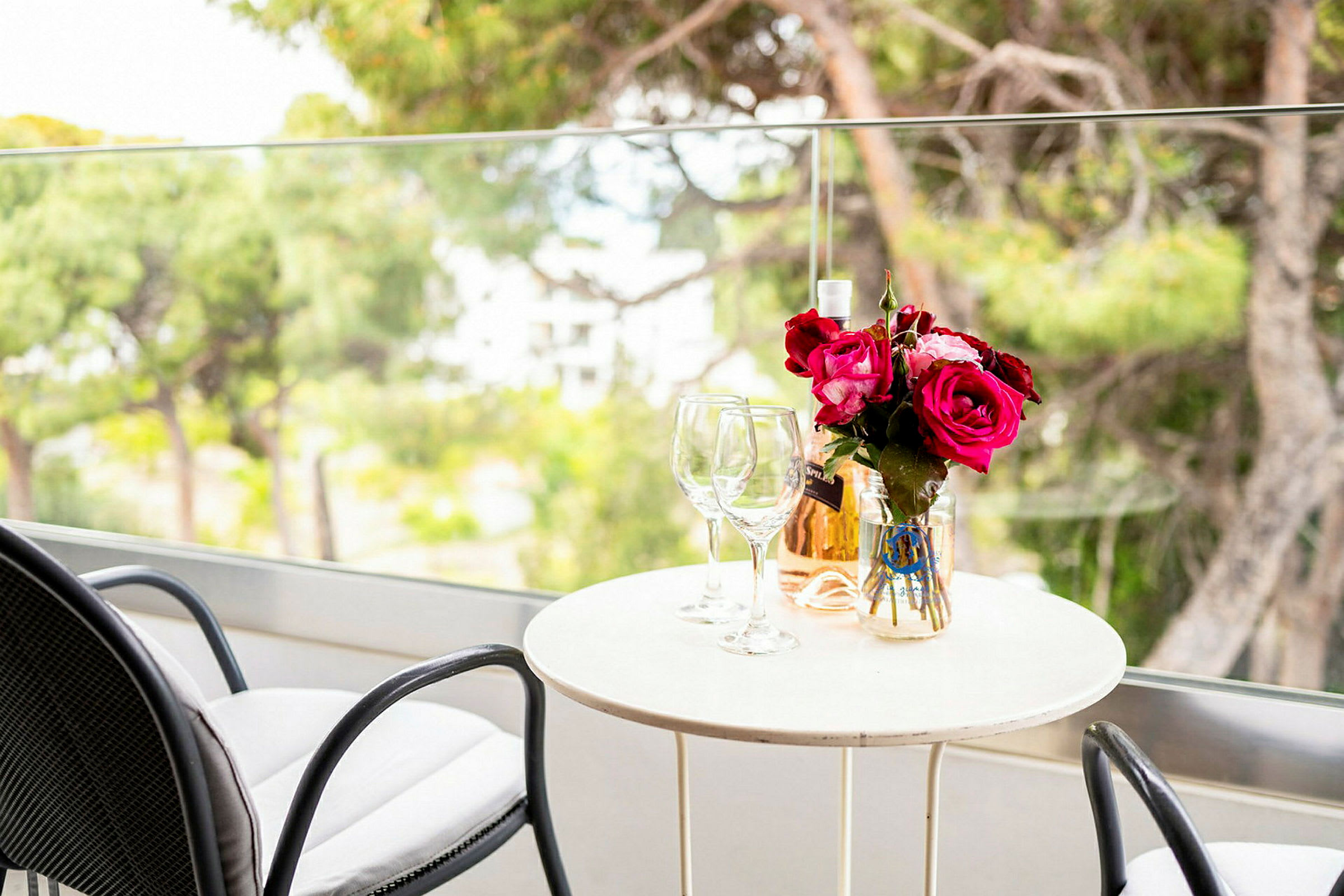 Ett bord med två glas, en vas med rosa blommor och en flaska rosévin på en balkong. (AI-genererad text)