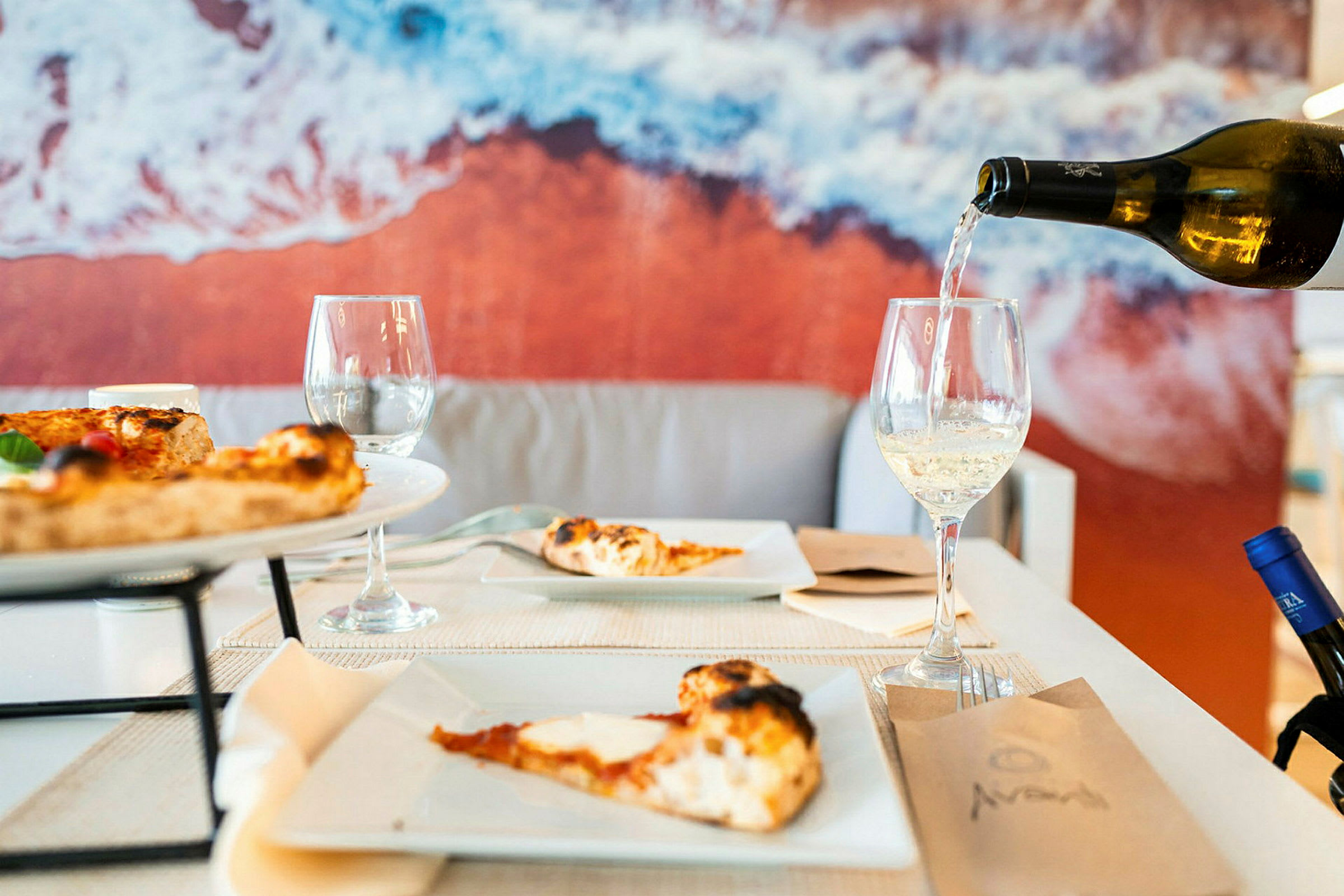Ett bord med pizza och vinglas, bakgrund med en bild av stranden. (AI-genererad text)