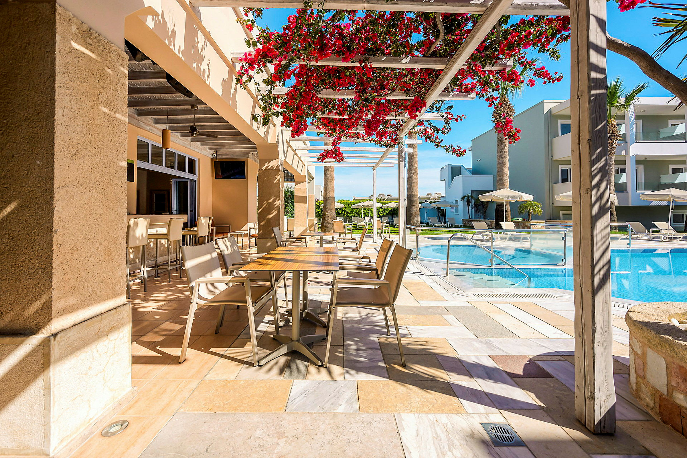 En uteservering med stolar och bord, nära en pool och omgiven av moderna byggnader. (AI-genererad text)