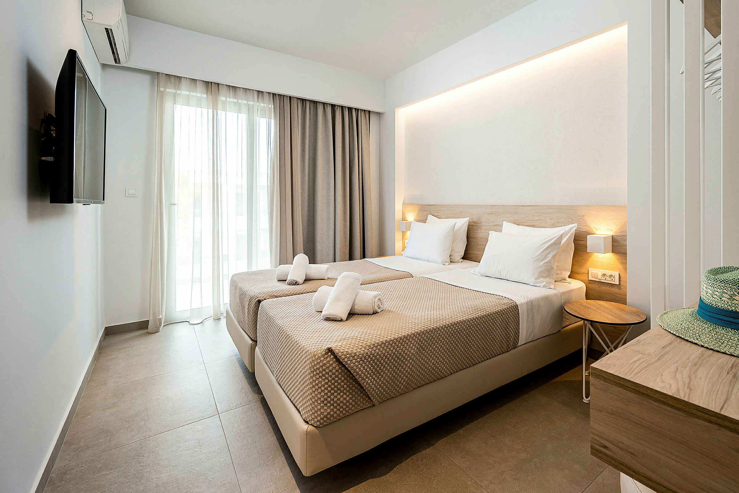 Ett hotellrum med två sängar bredvid varandra, tv och balkongdörr. (AI-genererad text)