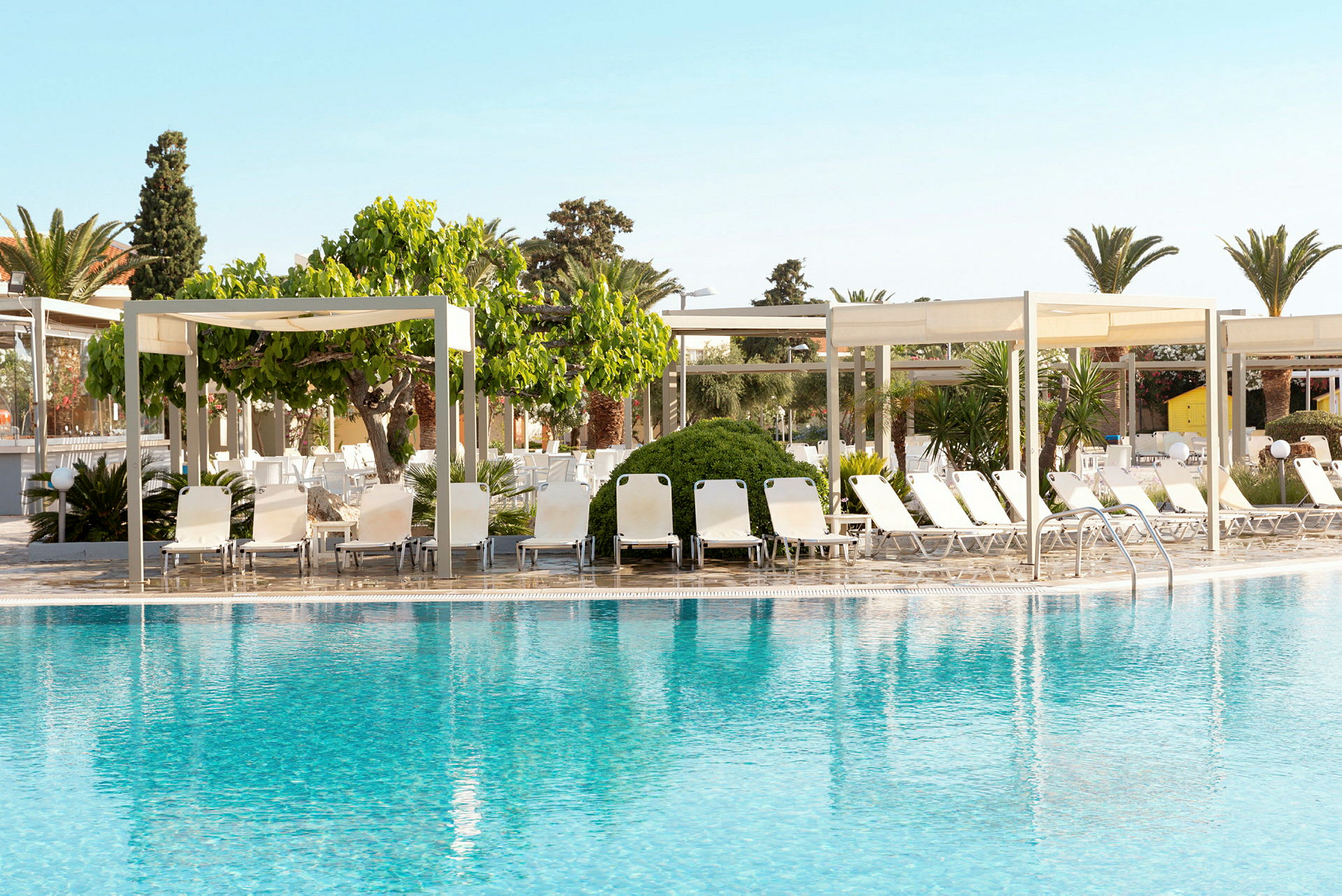 En pool med solstolar och skuggande paviljonger i bakgrunden. (AI-genererad text)