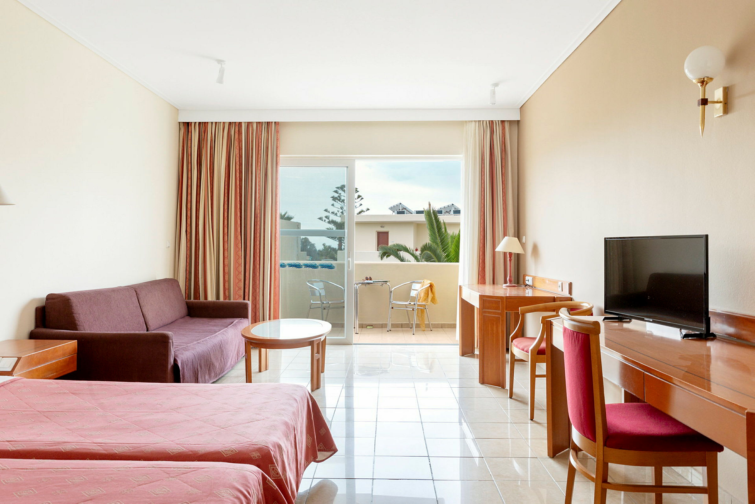 Ett hotellrum med två sängar, en soffa, ett bord, ett skrivbord med stol och en balkong med utsikt. (AI-genererad text)