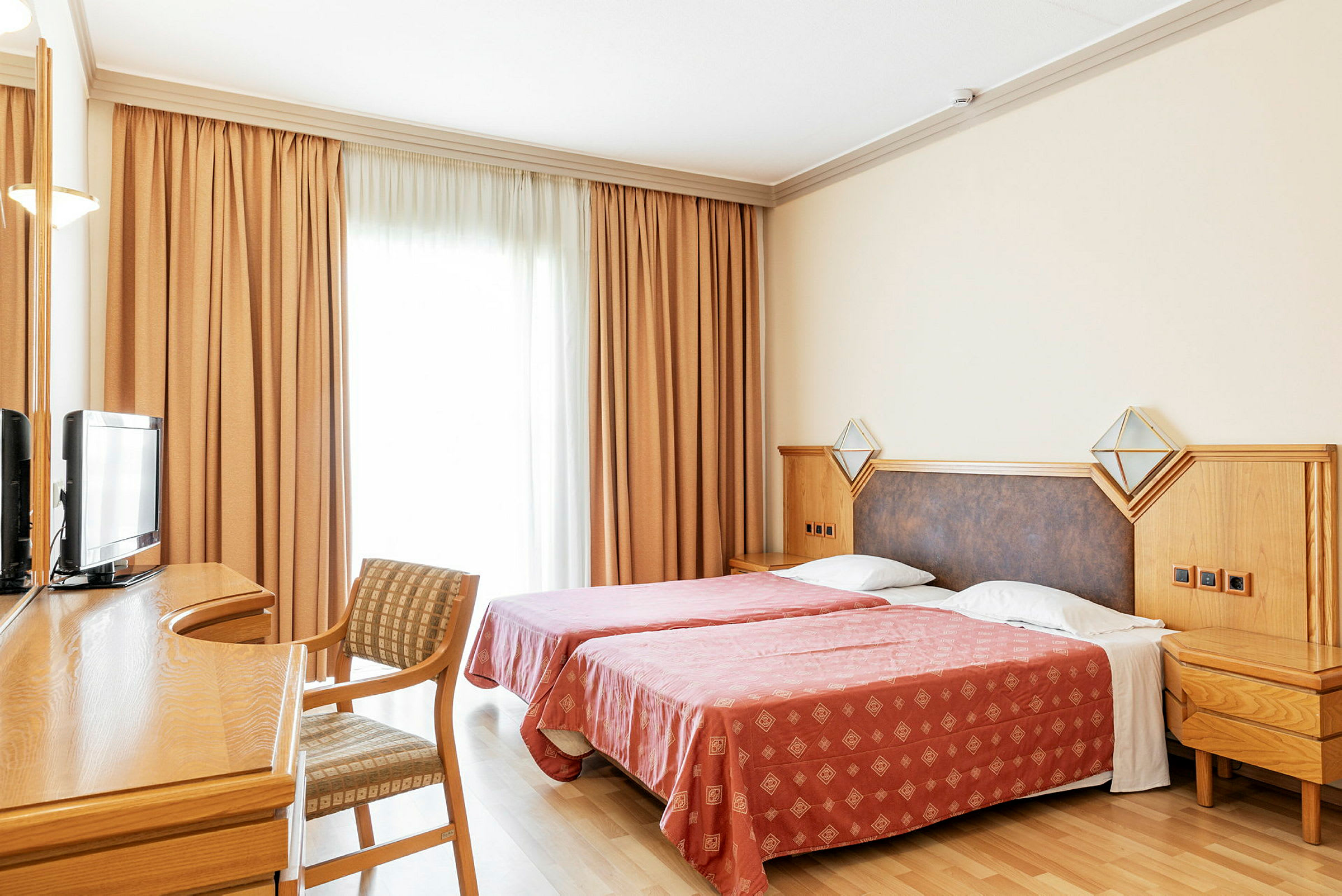 Hotellrum med två enkelsängar, skrivbord, stol och TV. (AI-genererad text)