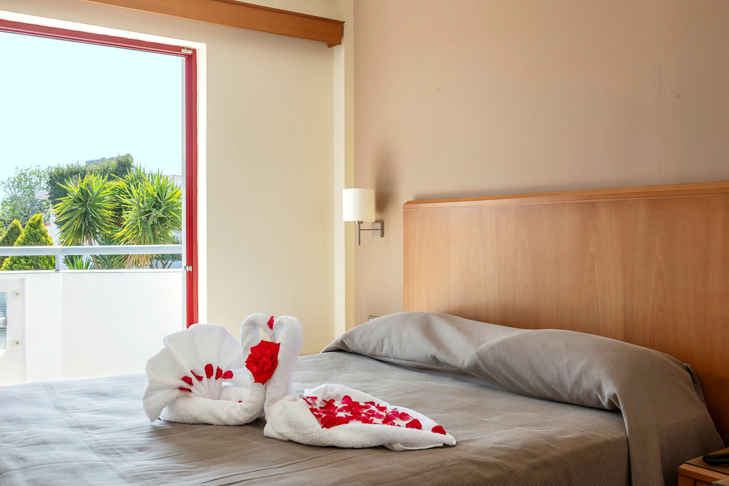Bild av en säng i ett hotellrum med en handduksvikning formad som svanar dekorerad med röda rosenblad. (AI-genererad text)