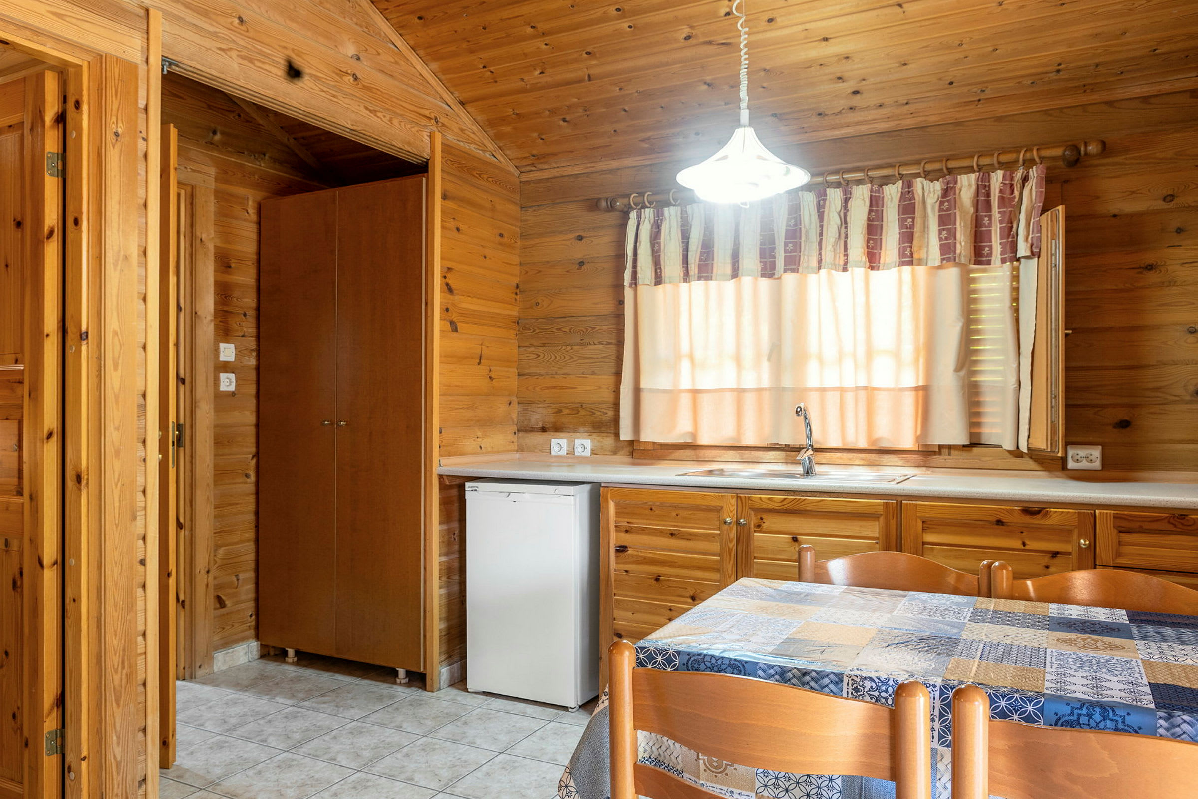 Inomhusmiljö med träpaneler, en diskbänk med kran, ett fönster med gardin och ett bord med stolar. (AI-genererad text)