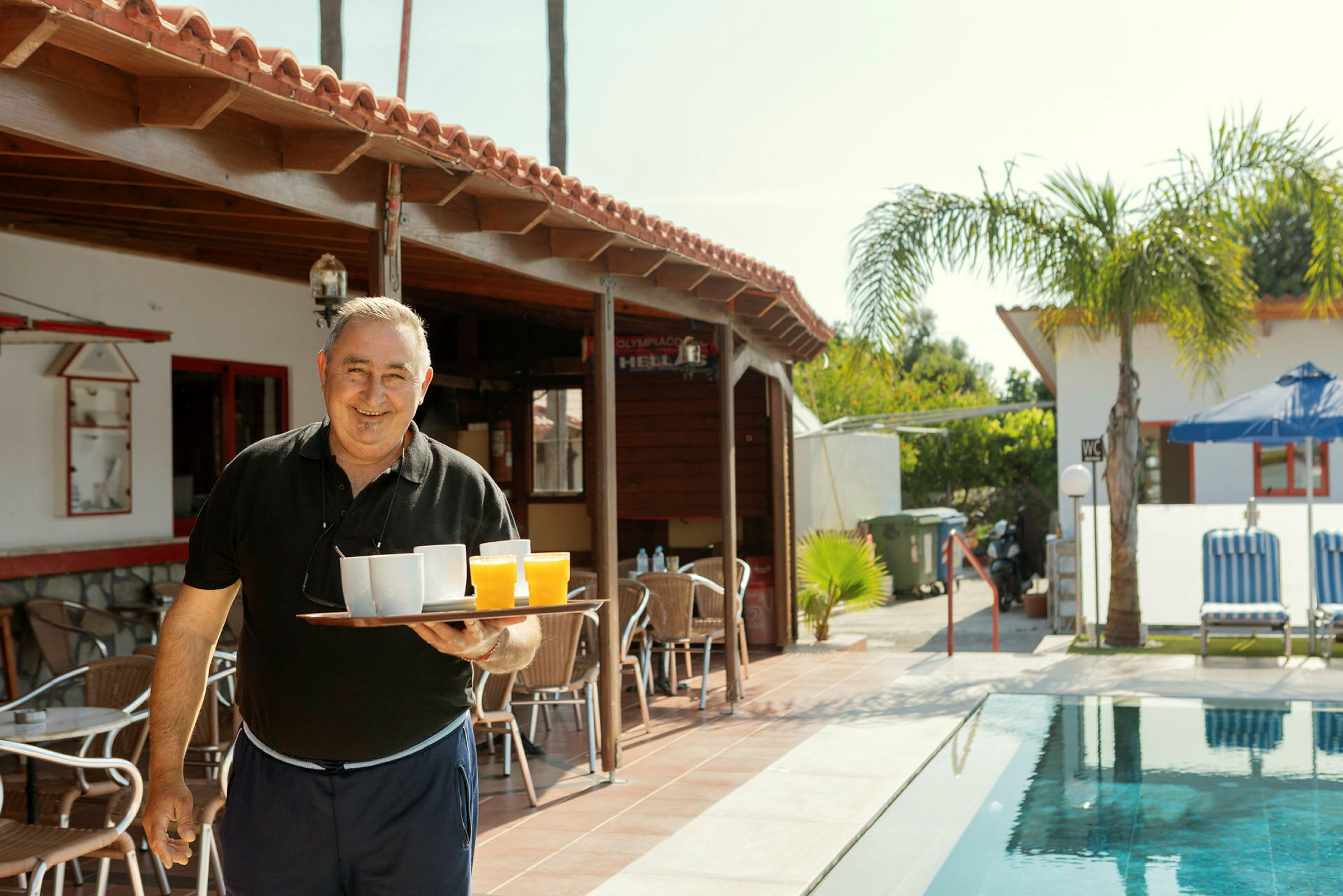Person bär en bricka med drycker vid en utomhuscafé nära en pool. (AI-genererad text)