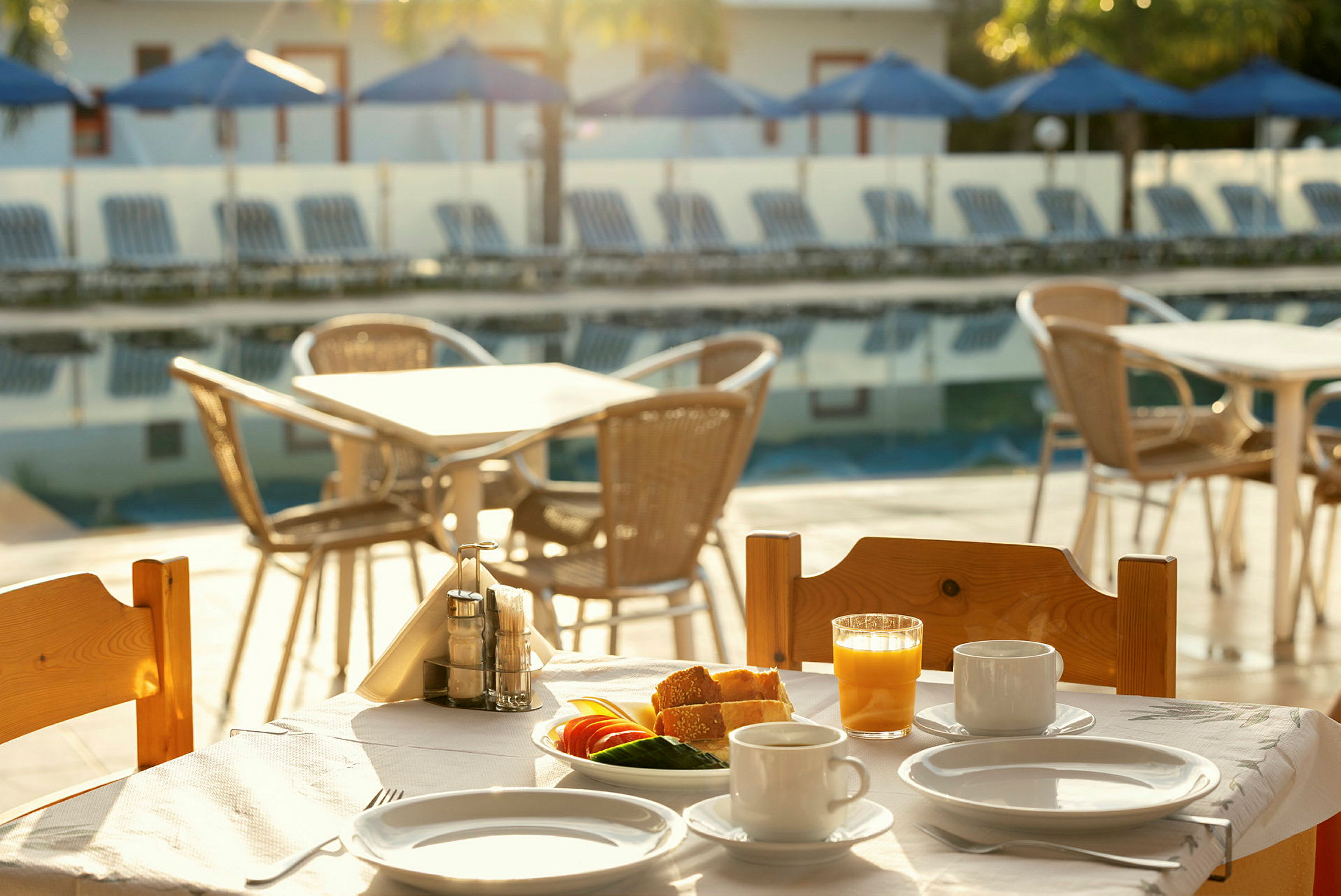Ett frukostbord vid en swimmingpool med serviser, juice och grönsaker. (AI-genererad text)