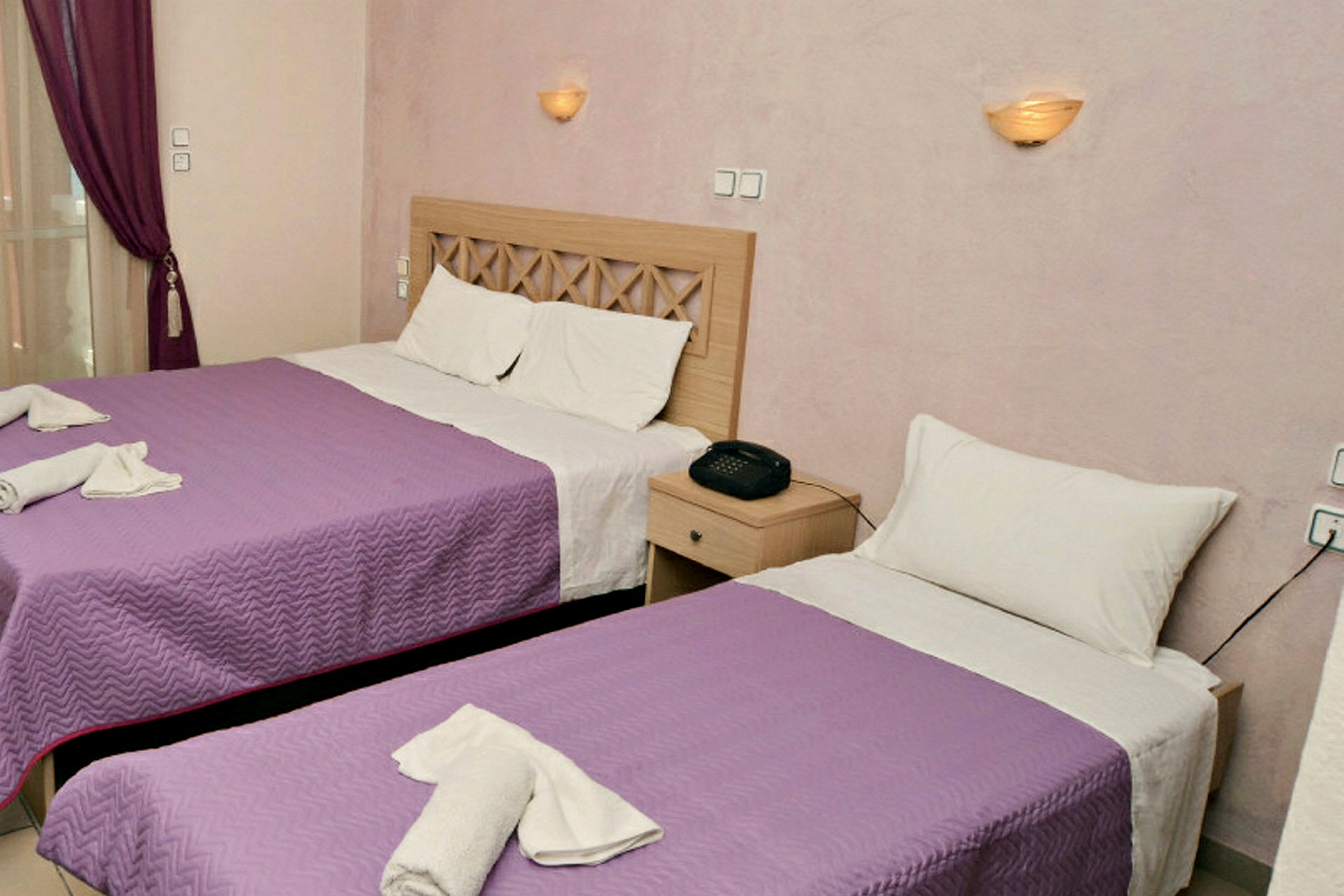 Ett hotellrum med två sängar med lila överkast, vita kuddar och ett nattygsbord med en telefon. (AI-genererad text)