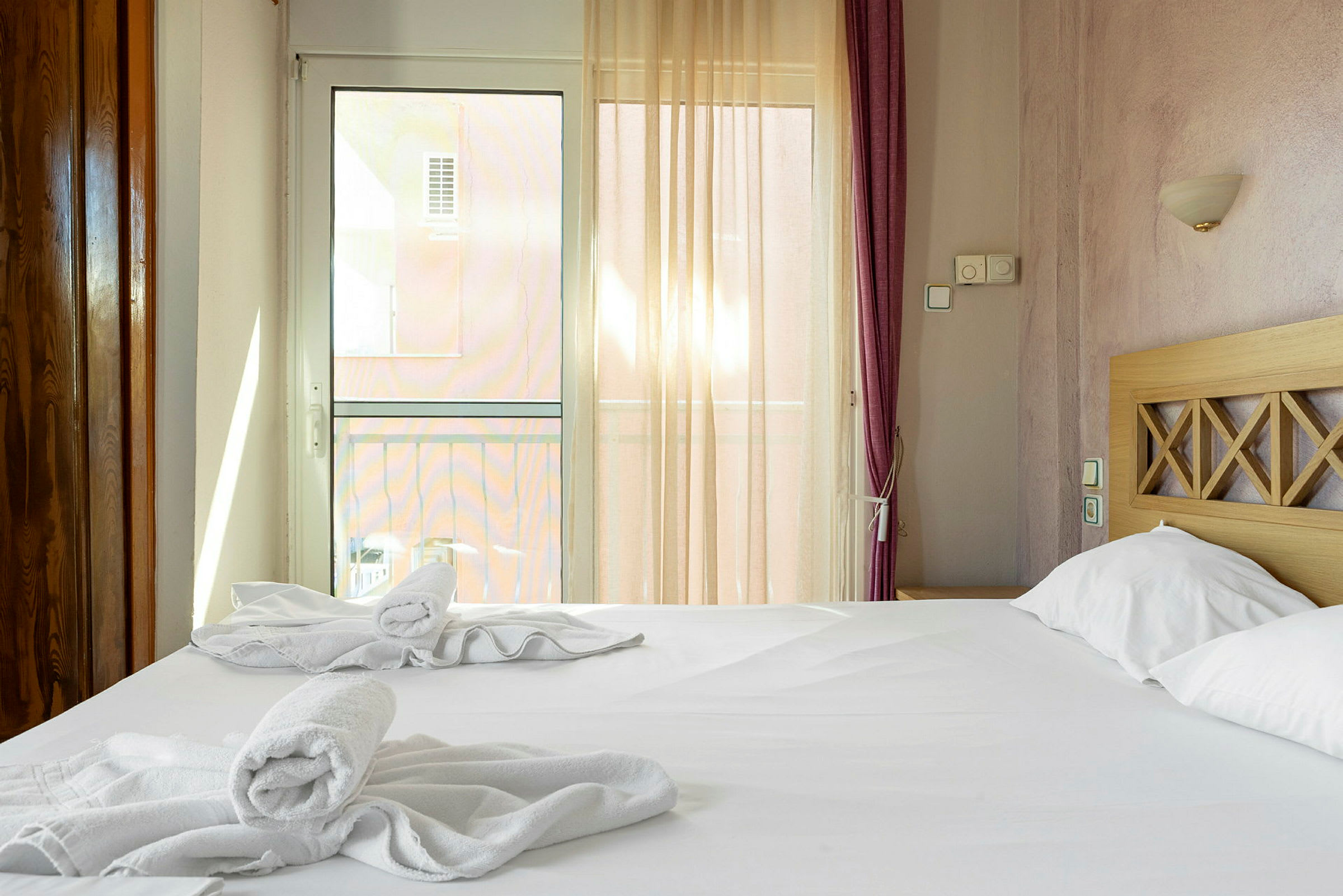 Ett hotellrum med en dubbelsäng, uppställda handdukar och ljusinsläpp genom en glasdörr. (AI-genererad text)