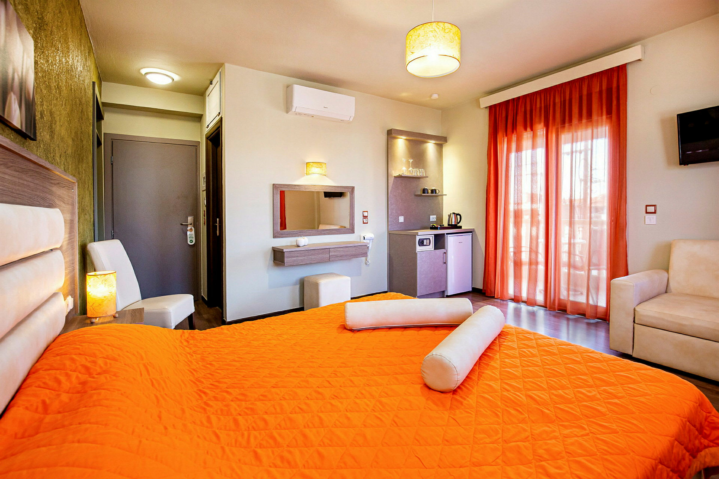 Ett hotellrum med en orange sängöverkast, vita möbler och en liten köksdel. (AI-genererad text)