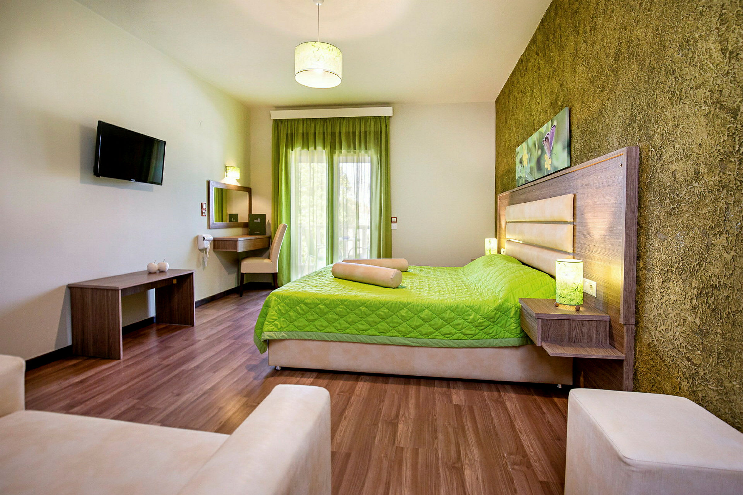 Ett hotellrum med en säng klädd i grönt överkast, skrivbord med stol, och en väggmonterad TV. (AI-genererad text)