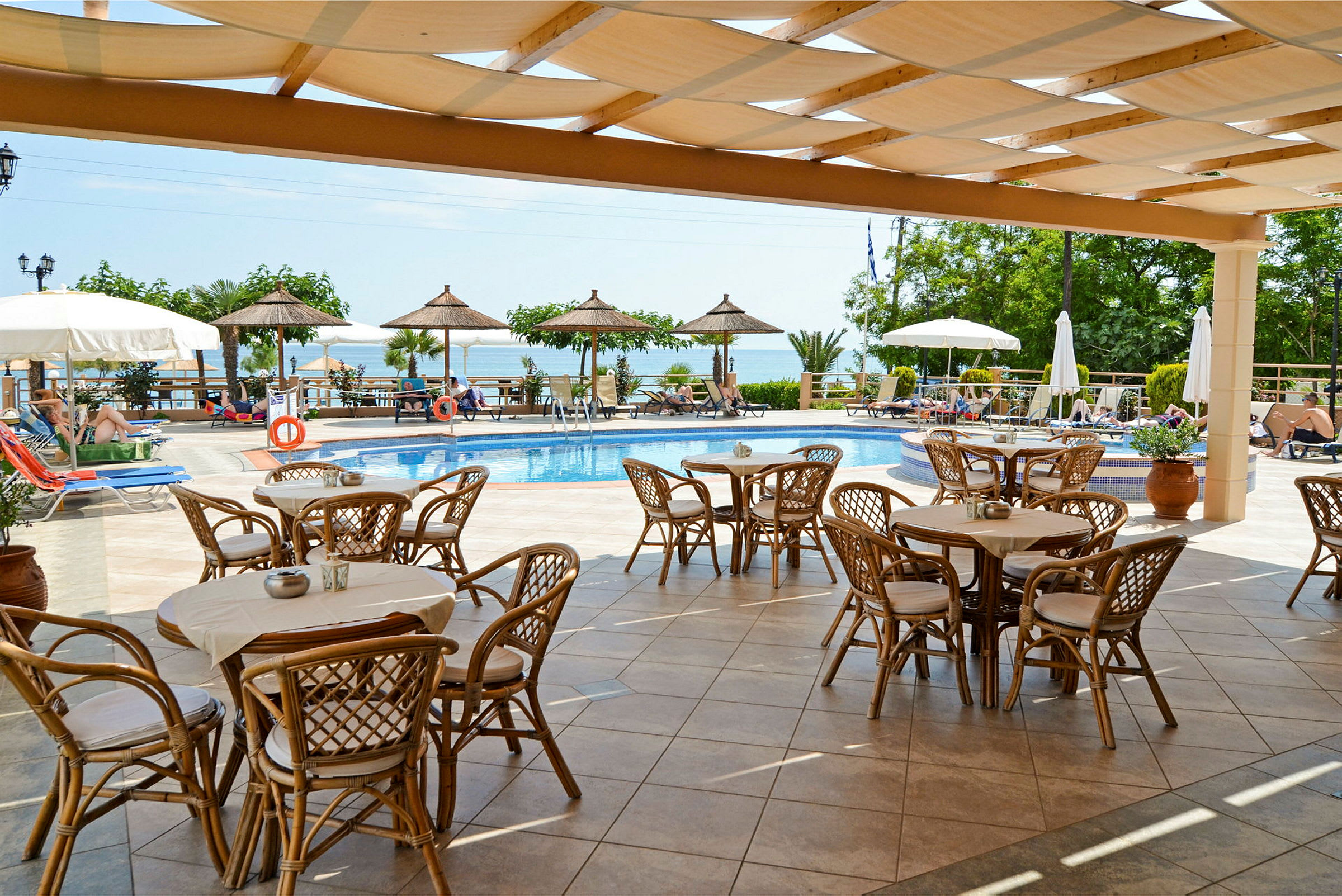 Utomhusområde med pool, bord och stolar under en pergola, och parasoller runt poolen. (AI-genererad text)