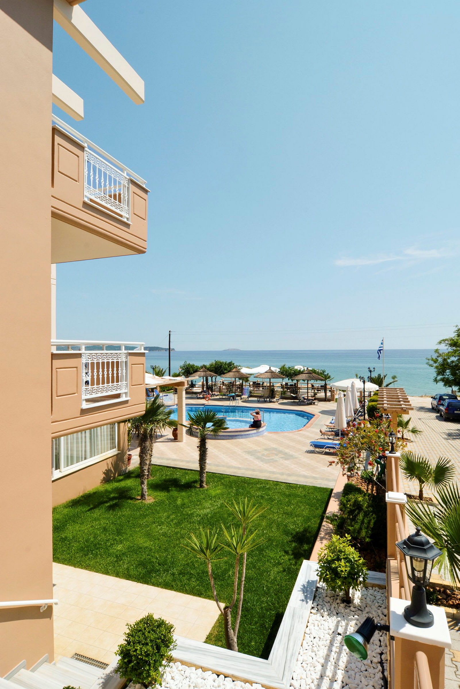 Utsikt över hotellområde med grön gräsmatta, pool och hav i bakgrunden. (AI-genererad text)