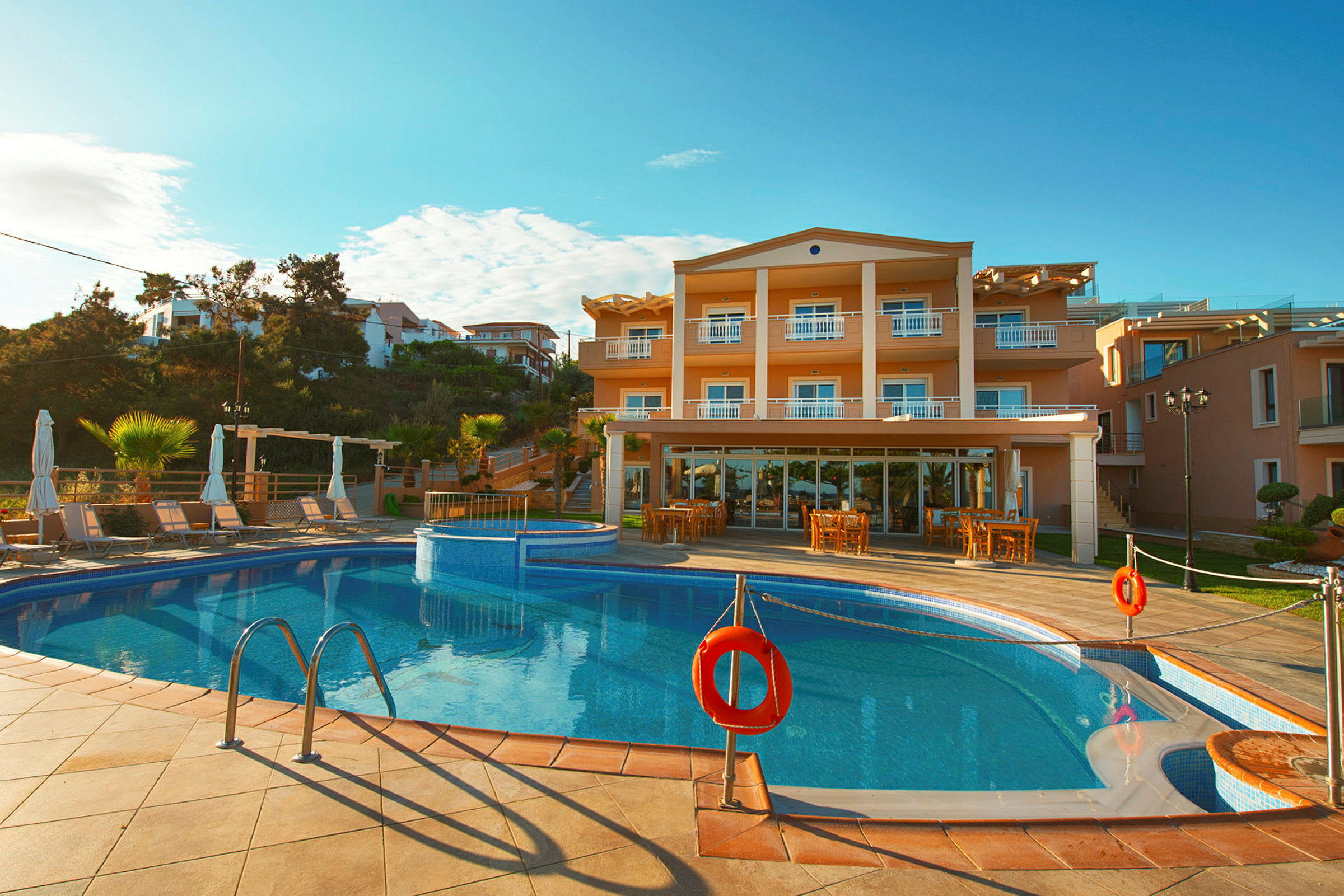 Bild av ett hotell med tre våningar, framför vilket finns en pool med solstolar runtom. (AI-genererad text)