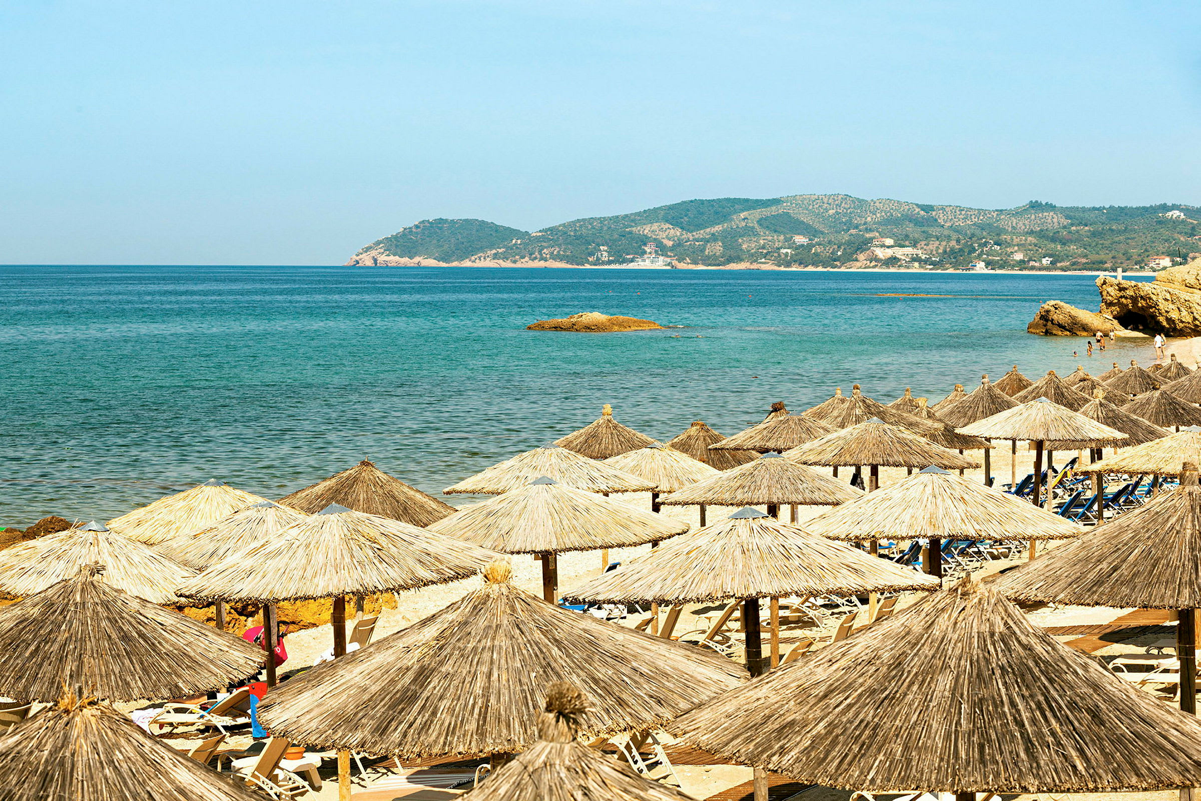 Strand med parasoller, solstolar, hav och berg. (AI-genererad text)