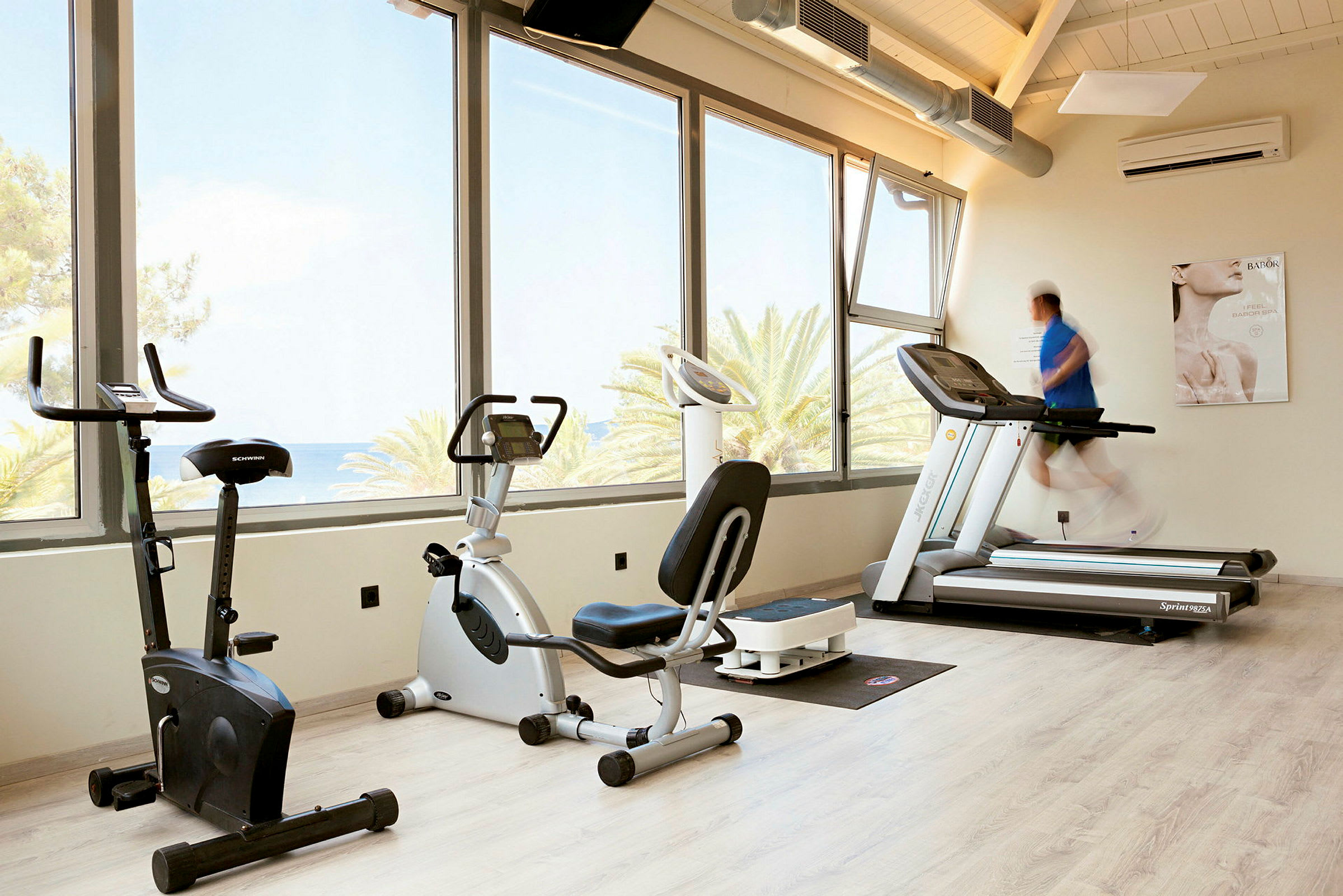 Ett gym med träningscyklar och löpband vid fönster med utsikt. (AI-genererad text)