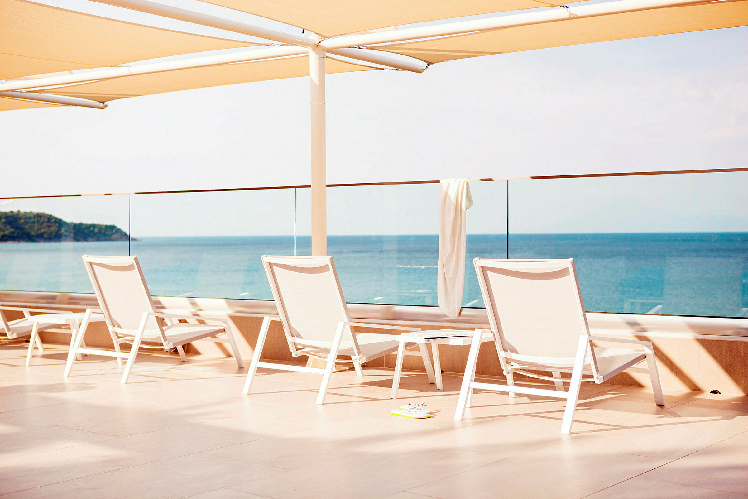 Solstolar och bord på en terrass med utsikt över havet. (AI-genererad text)