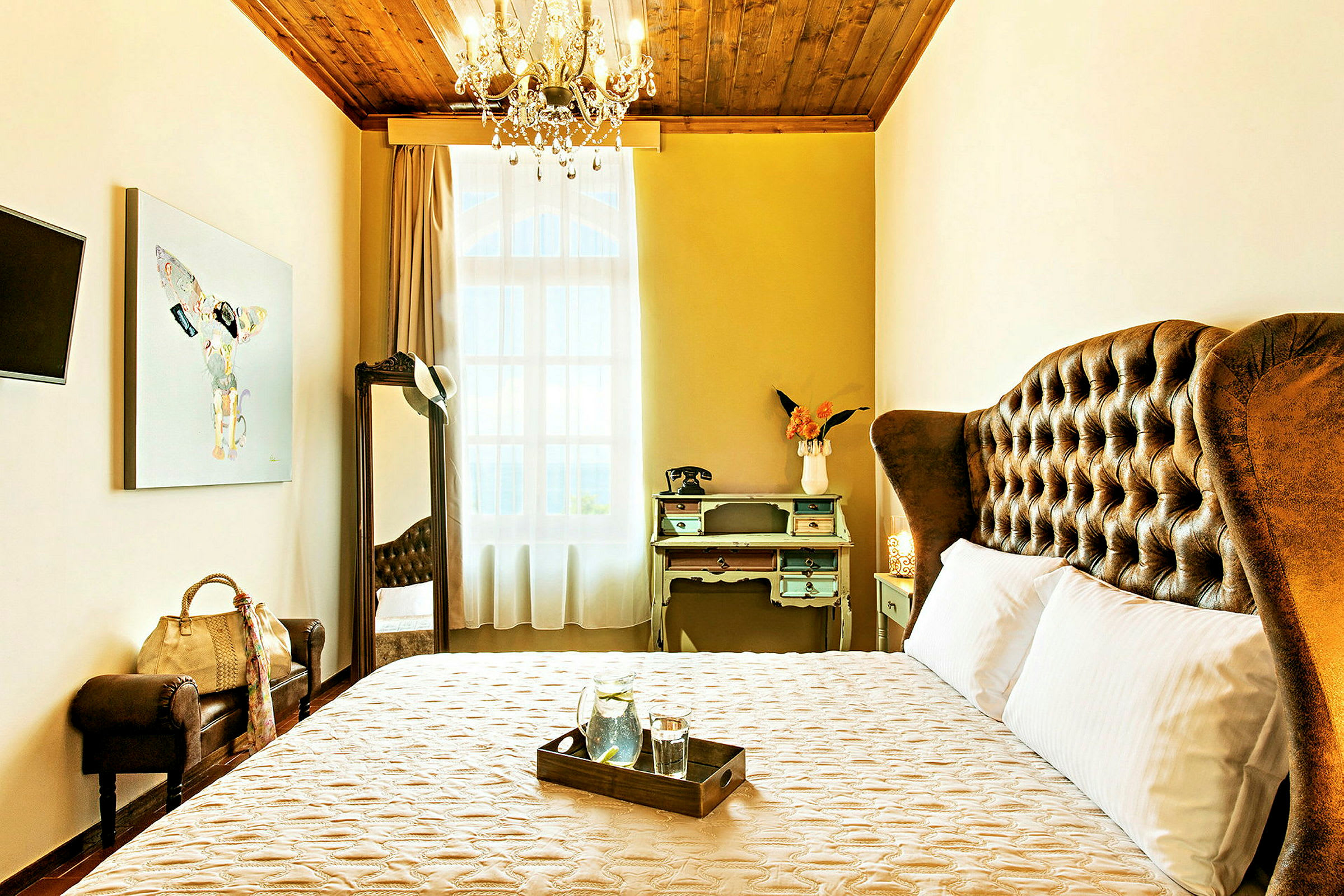 Ett elegant hotellrum med en stor säng, vintage skrivbord och dekorativ taklampa. (AI-genererad text)