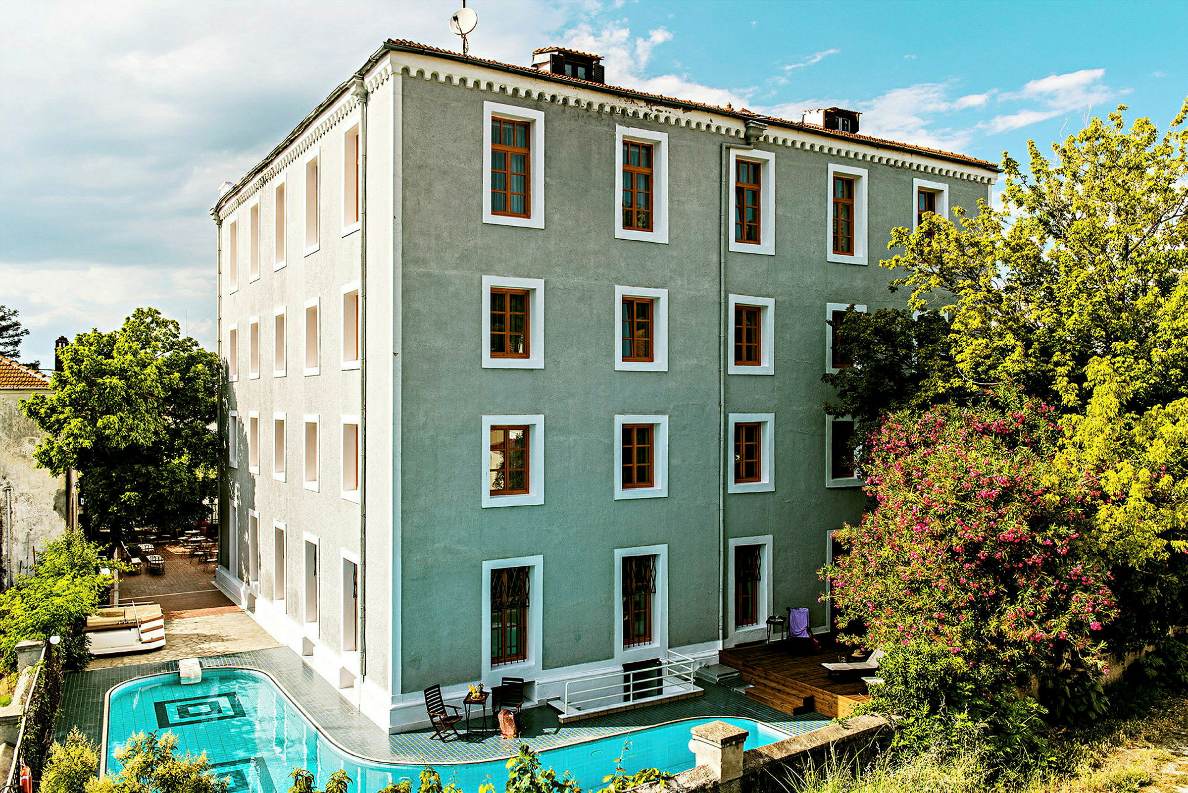 Byggnad med grönt fasad med en pool framför och omgivande grönska. (AI-genererad text)