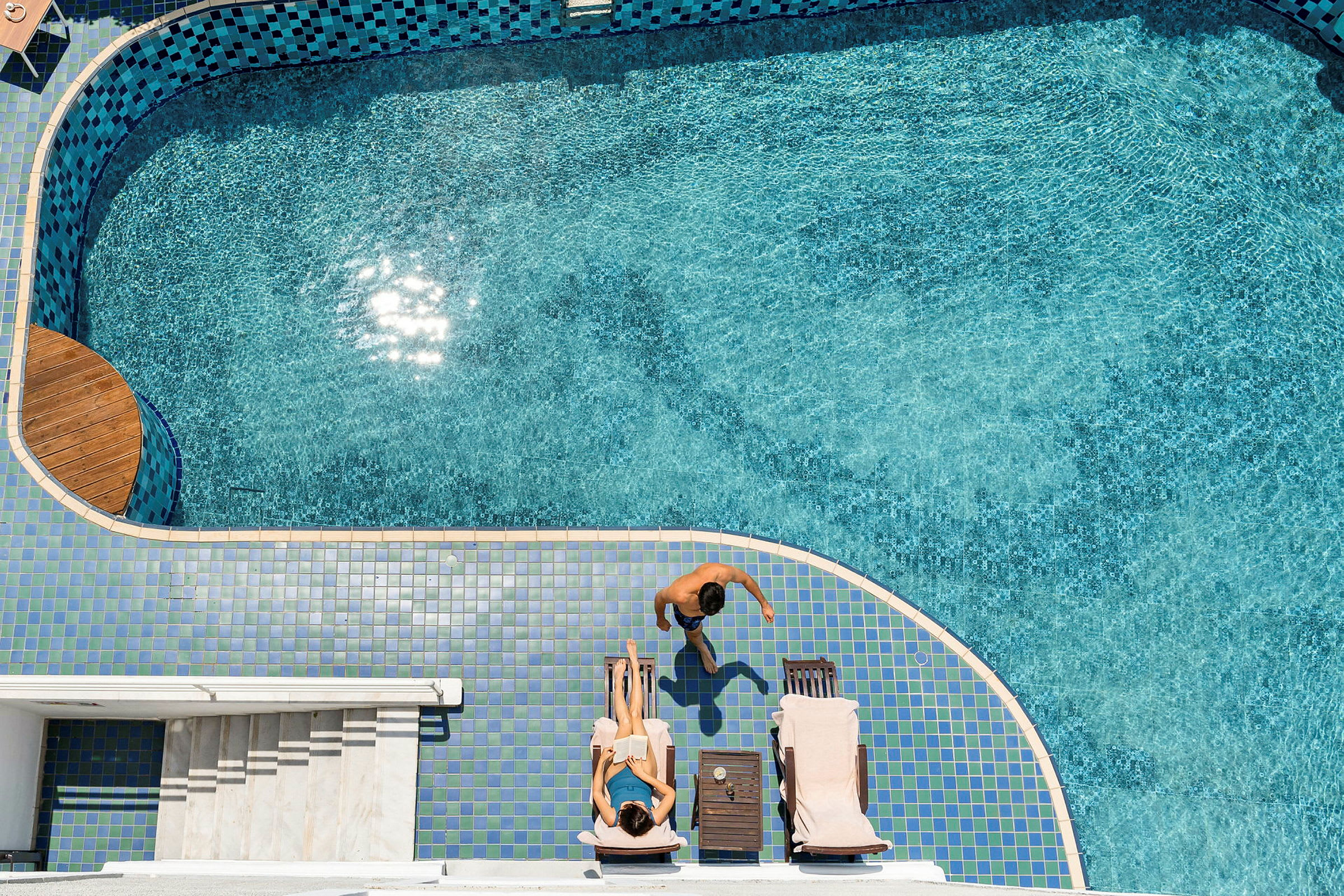 Personer vid en pool, en kvinna ligger på solstol och en man går intill. (AI-genererad text)