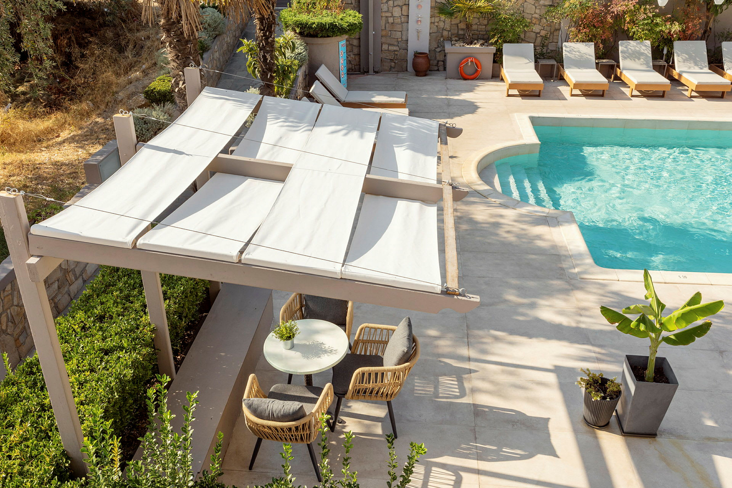 Bild visar en utomhuspool med solstolar och ett område med sittplatser under en pergola som erbjuder skugga. (AI-genererad text)