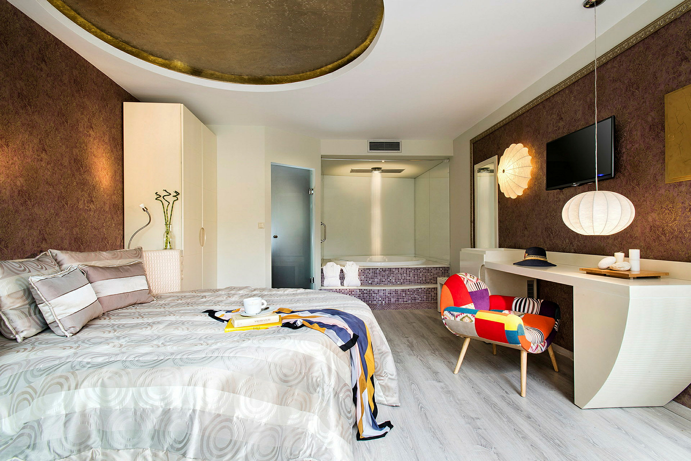 Ett modernt hotellrum med en dubbelsäng, färgglad stol och en jacuzzi i bakgrunden. (AI-genererad text)