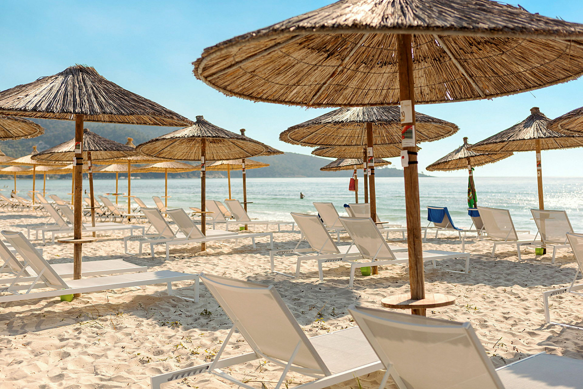 Strand med parasoller och solstolar, med havsutsikt i bakgrunden. (AI-genererad text)