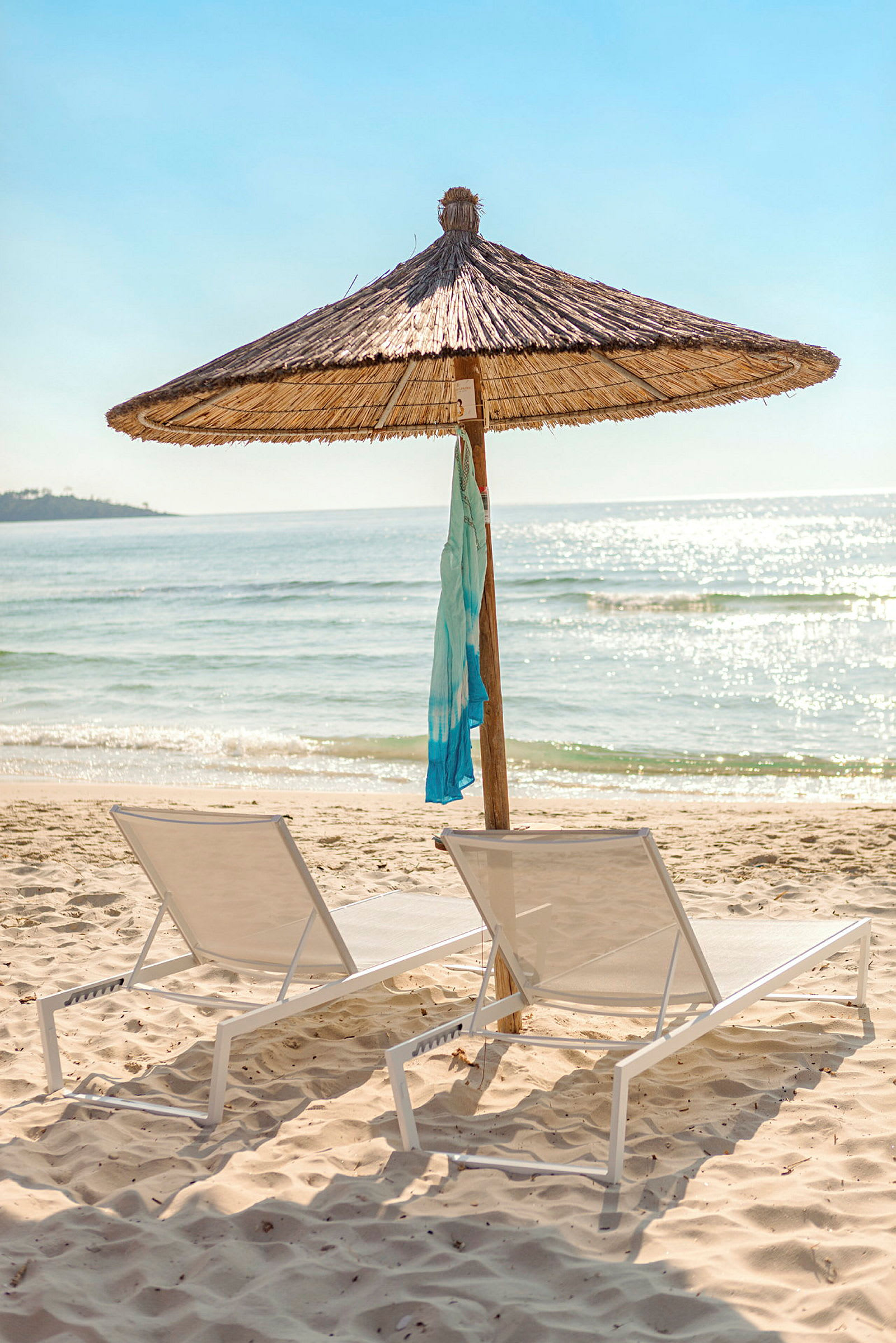 Två solstolar under ett parasoll på en sandstrand med havsutsikt. (AI-genererad text)
