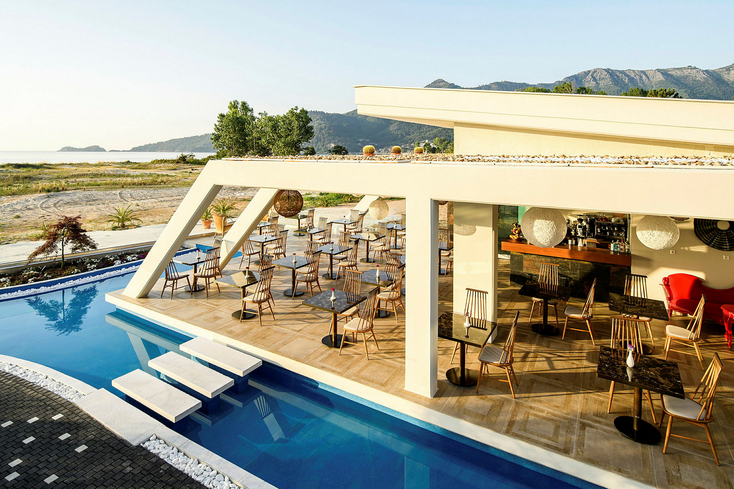 Uteservering vid en pool med stolar och bord, omgivna av grönska och berg i bakgrunden. (AI-genererad text)
