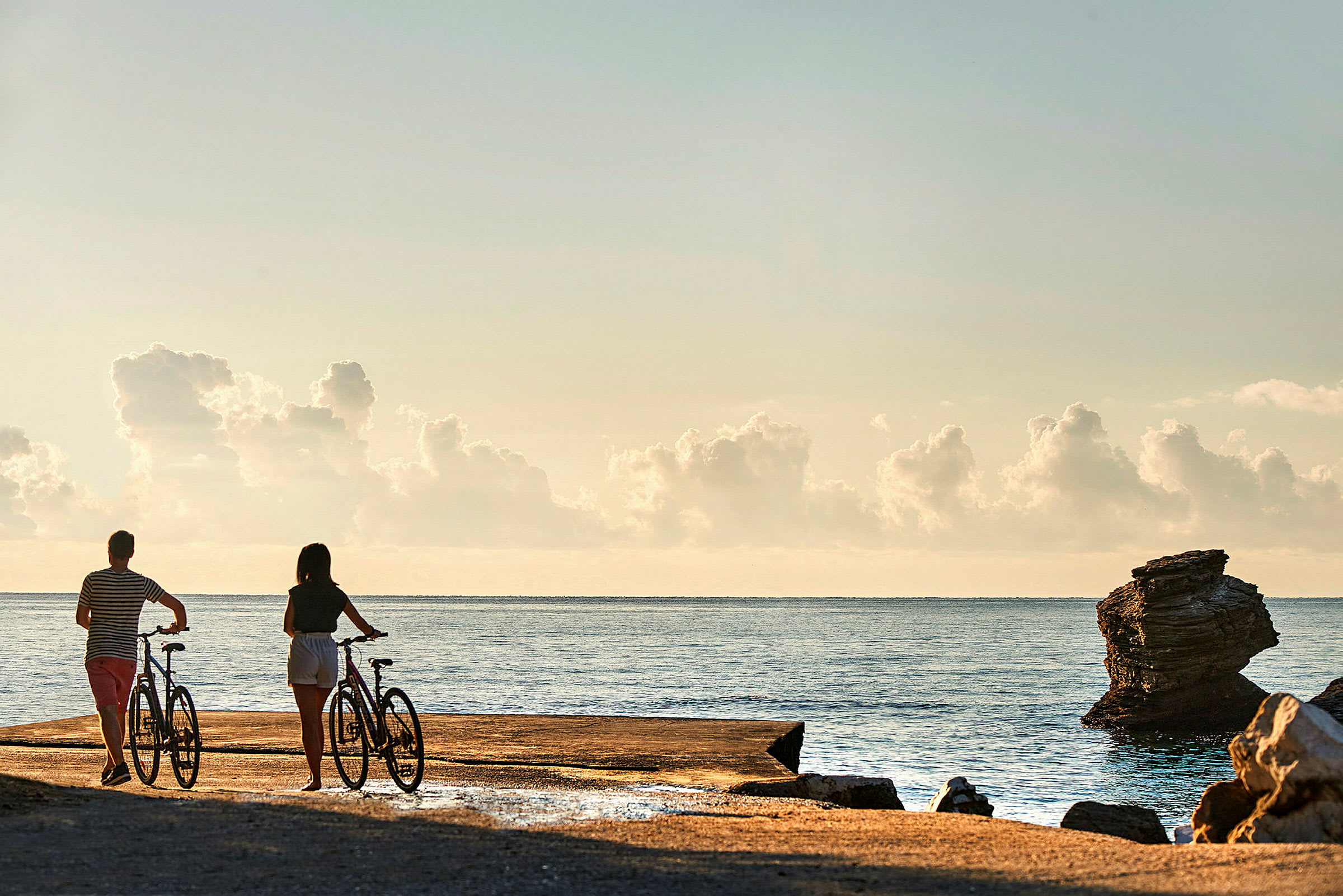 Två personer med cyklar vid havet under en klar himmel med moln. (AI-genererad text)