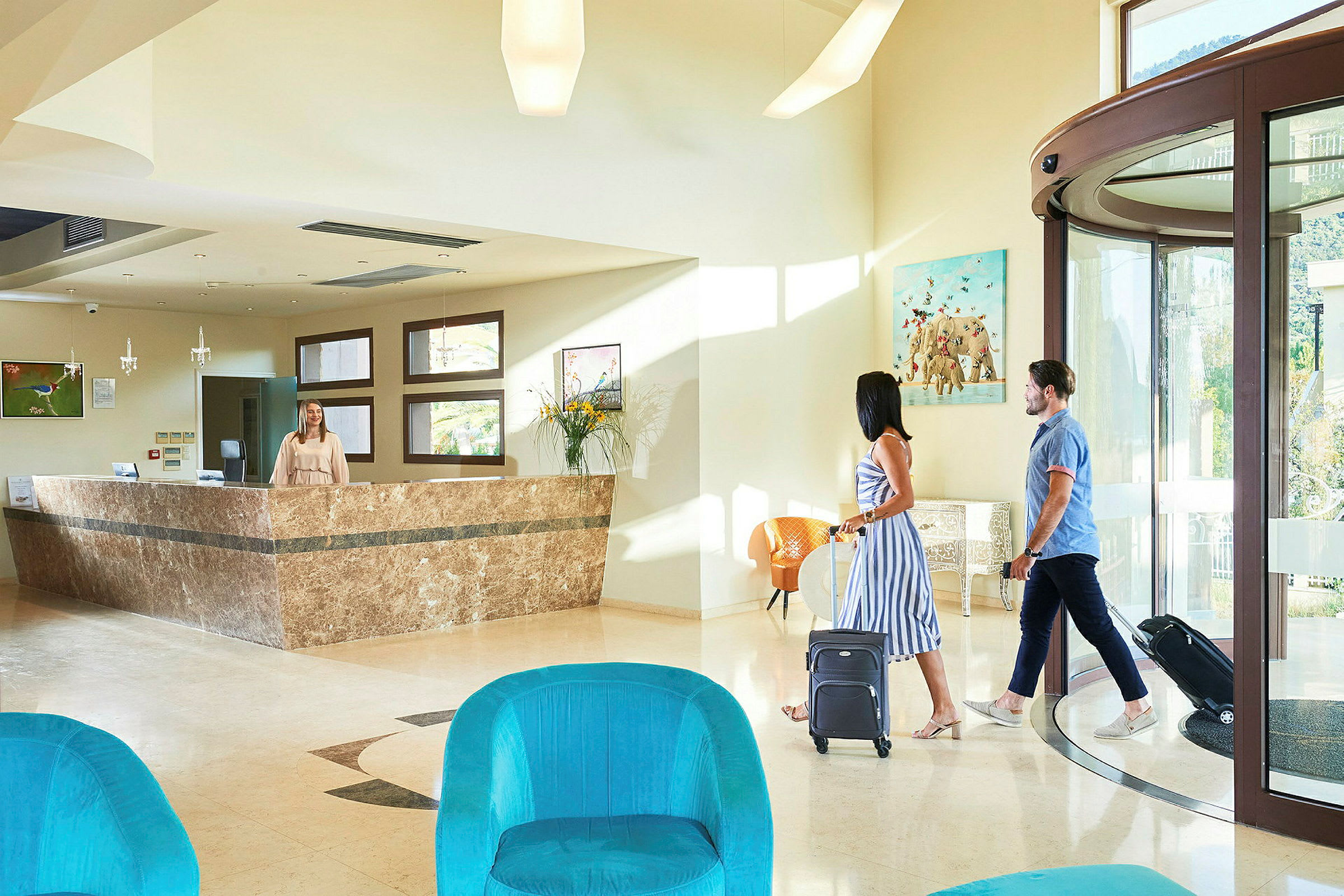 Ett ljust hotellobbyområde med reception och två personer som går in med resväskor. (AI-genererad text)