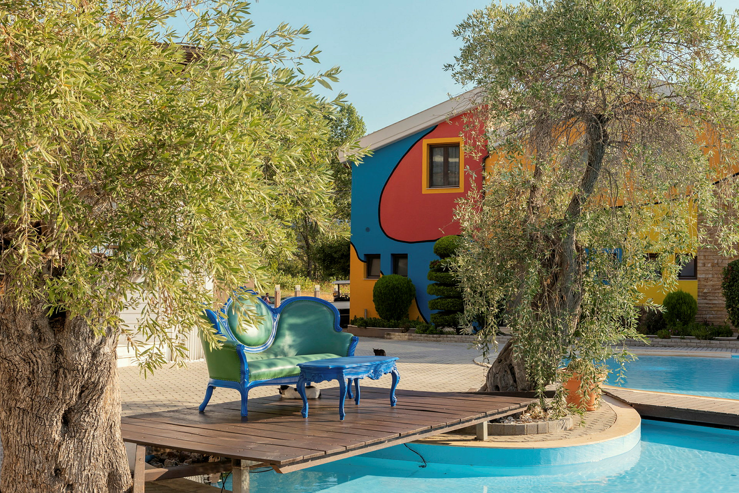 Ett färgglatt hus vid en pool med en grön soffa och ett blått bord på en träterrass. (AI-genererad text)