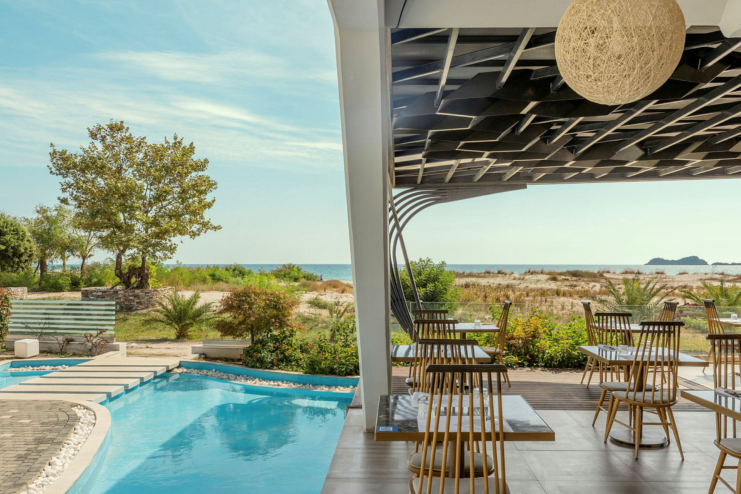 En terrass med bord och stolar, en pool och grönska framför havet. (AI-genererad text)