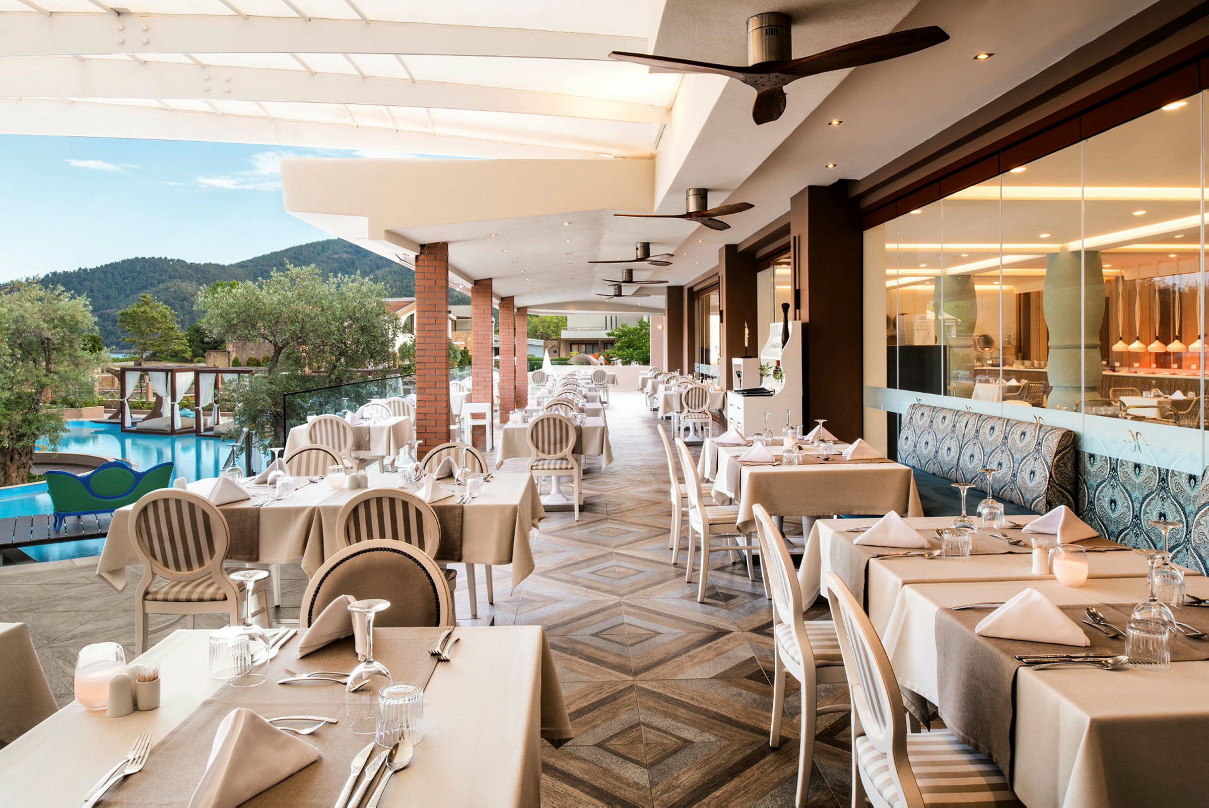 Restaurang med dukade bord, utsikt över pool och grönska. (AI-genererad text)