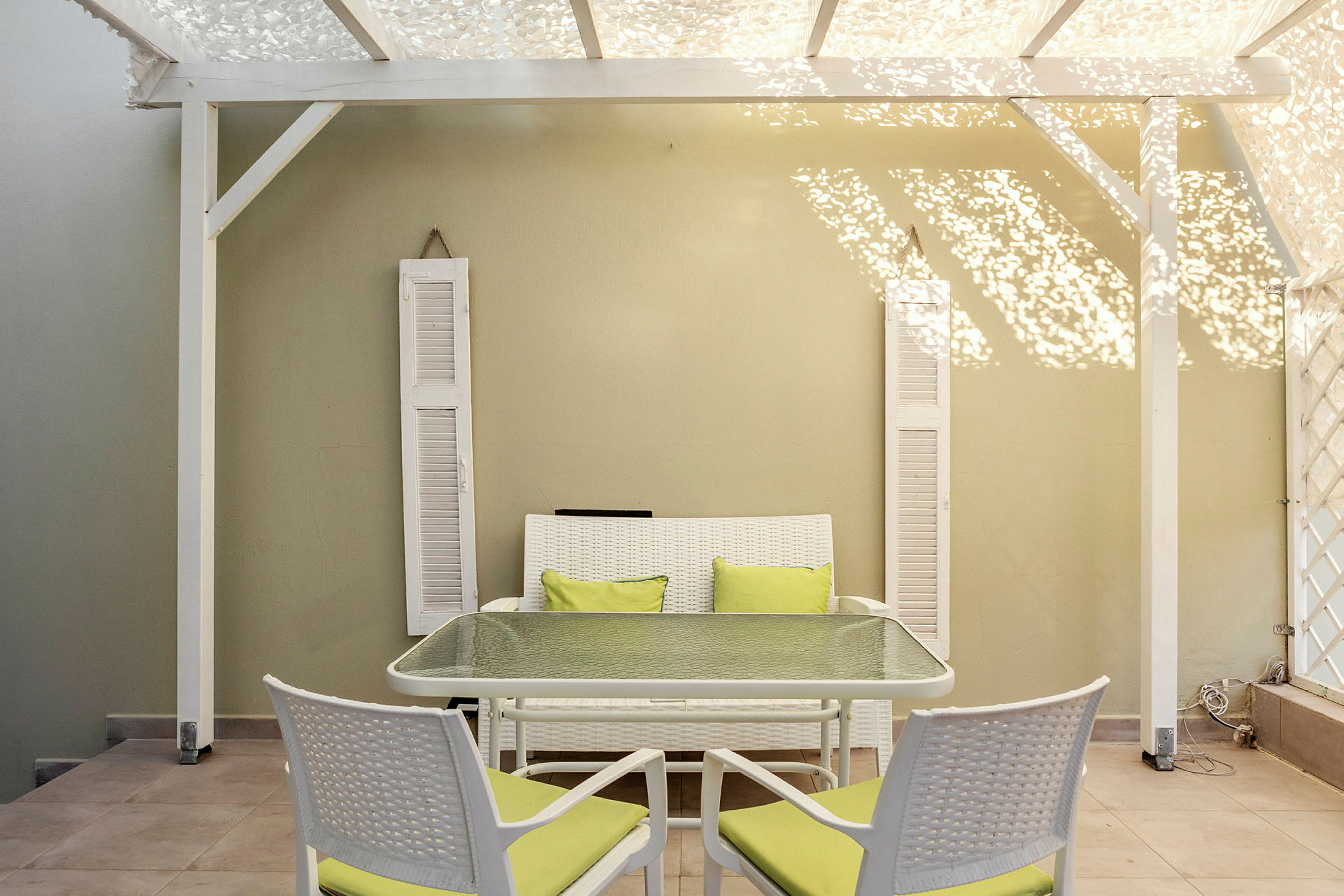 Trädgårdsmöbler med grönvita sittdynor under en vit pergola. (AI-genererad text)
