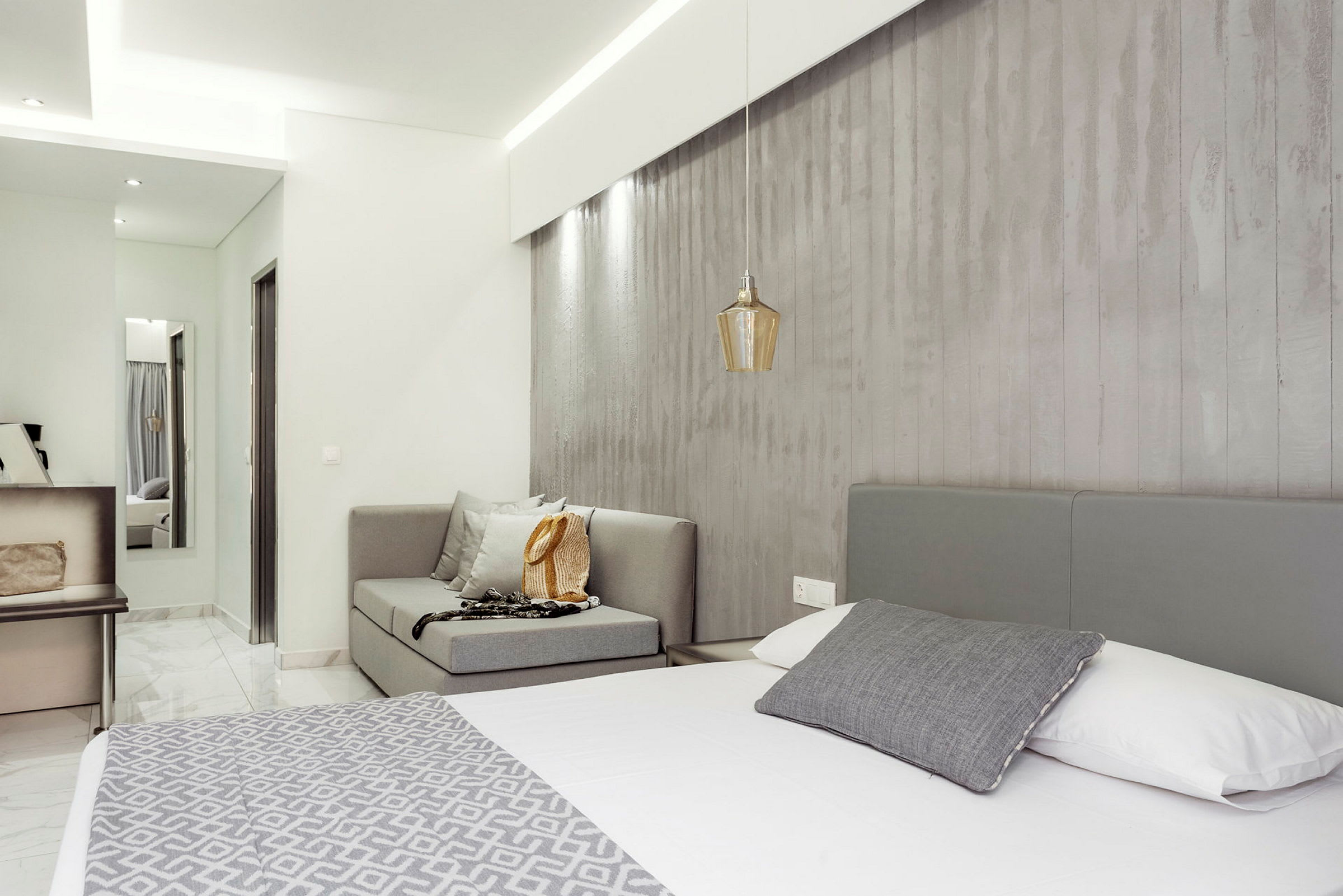 Ett modernt inrett hotellrum med en grå säng, soffa och ljus inredning. (AI-genererad text)