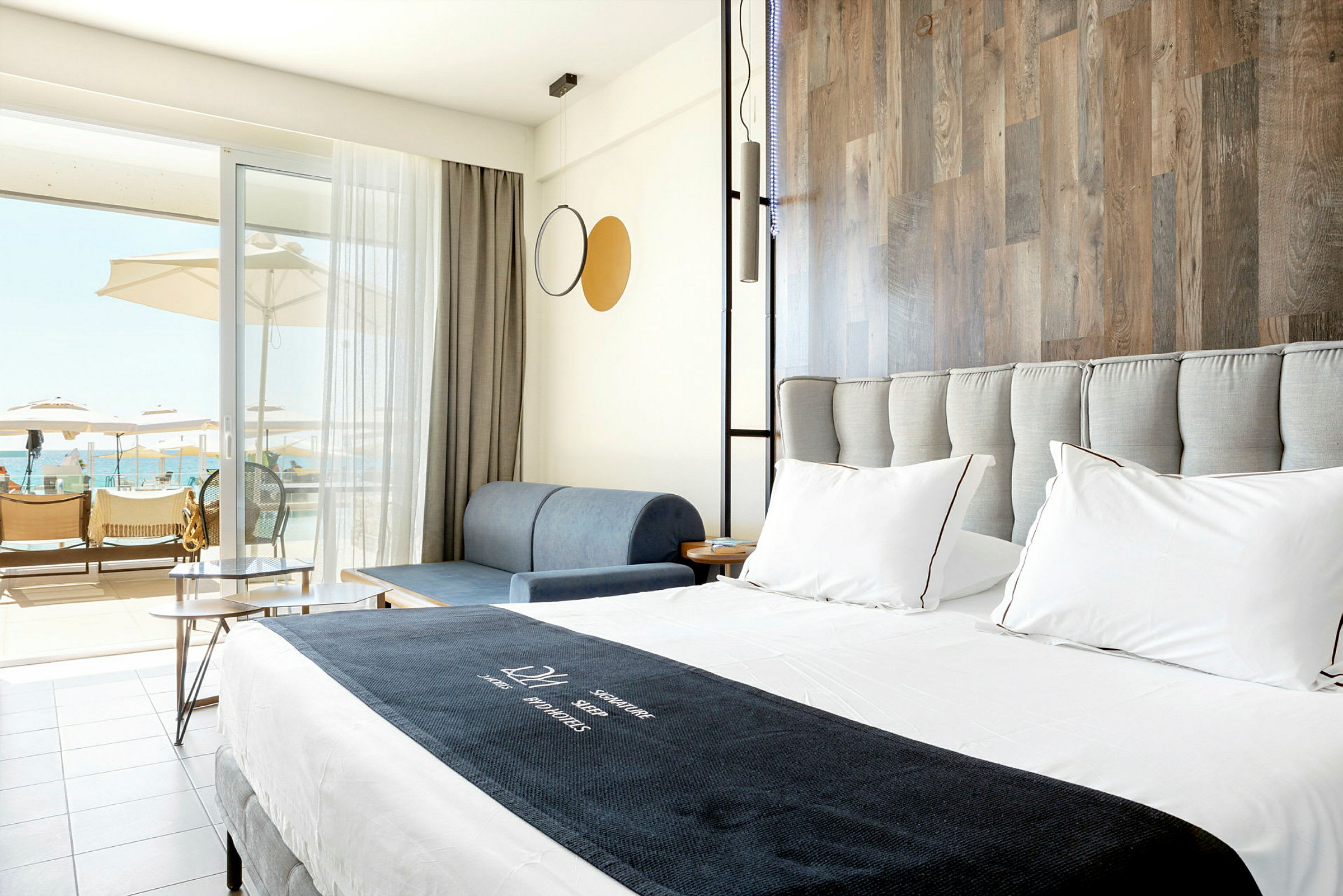 Ett ljust hotellrum med dubbelsäng, soffa och balkong med utsikt över poolområdet. (AI-genererad text)