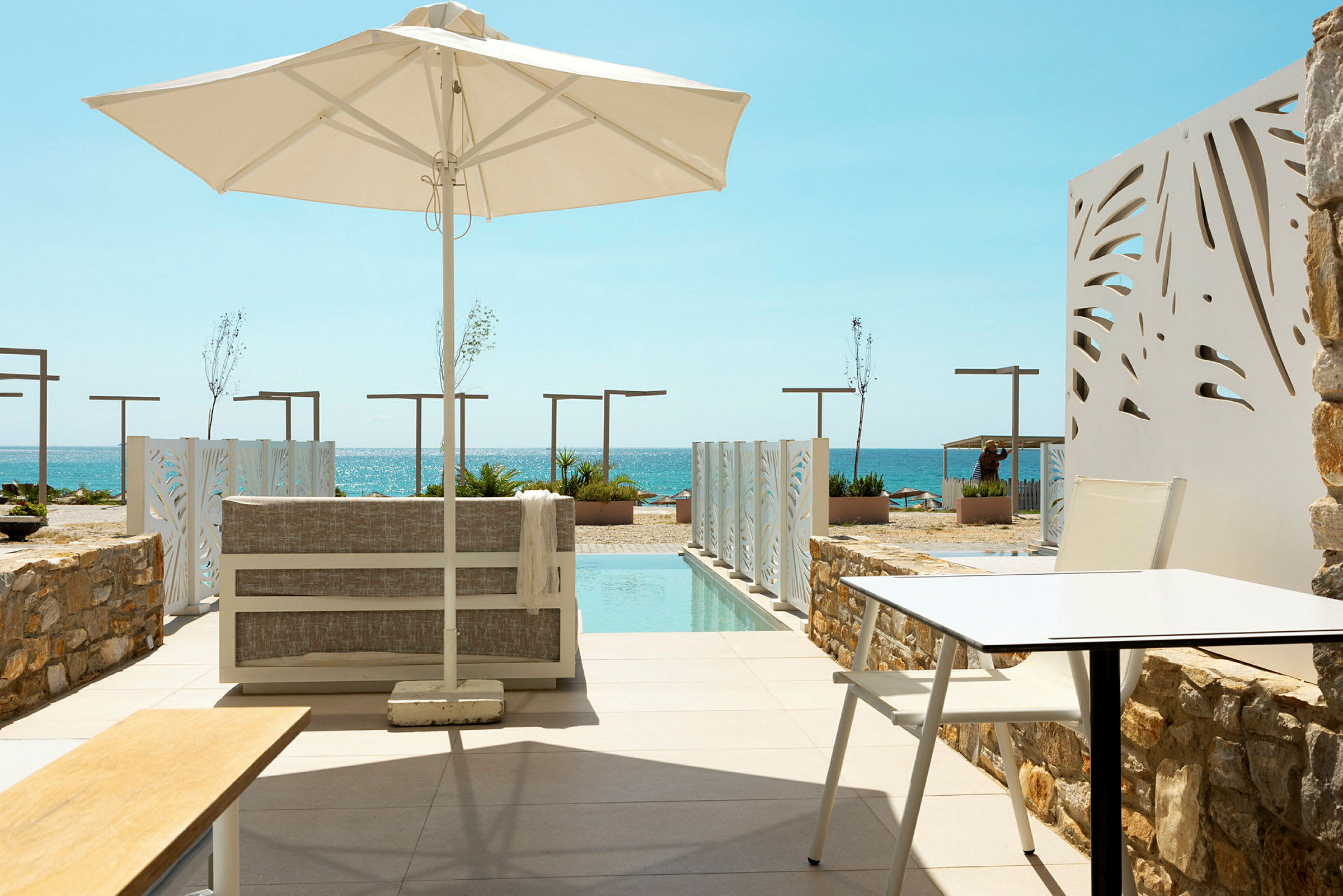 Terrass med sittmöbler och parasoll vid en pool, med utsikt mot havet. (AI-genererad text)