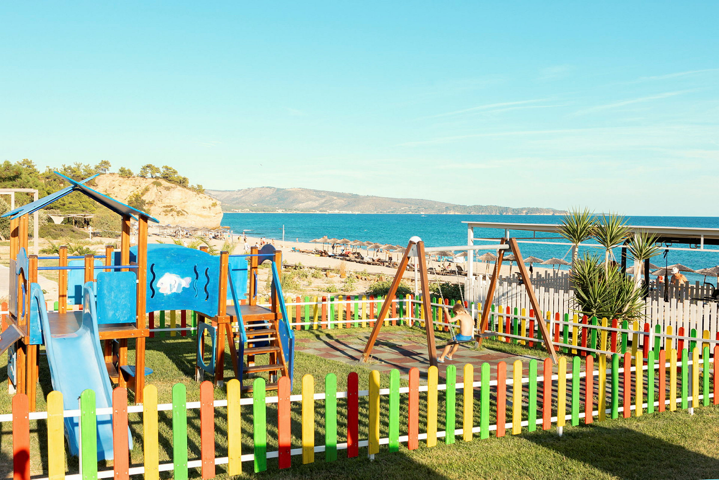 Lekplats med färgglada staket nära en strand och havsutsikt. (AI-genererad text)