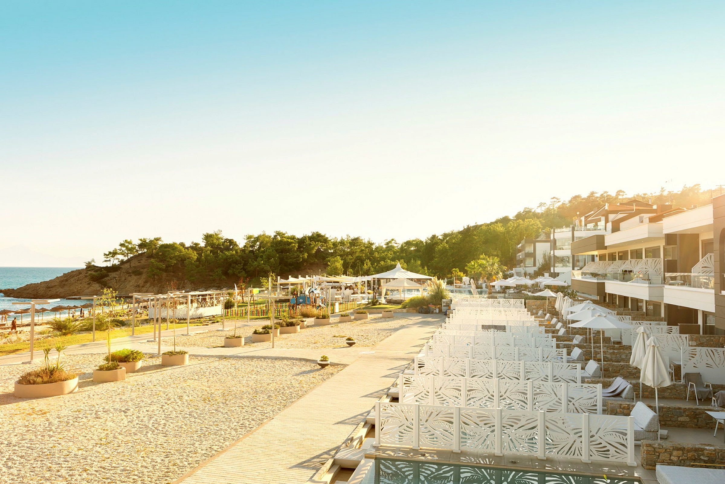 Ett hotellområde med pooler, solstolar och parasoller framför havet och omgivande grönska. (AI-genererad text)