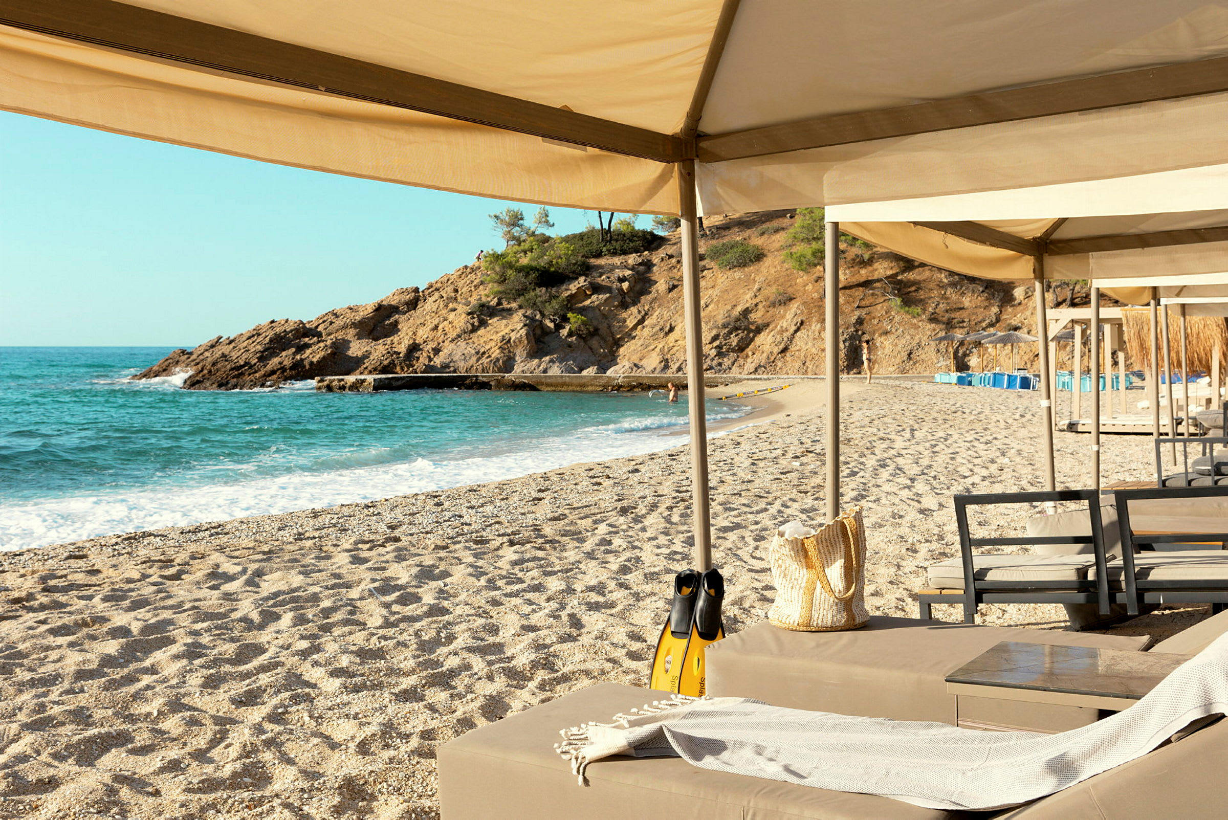 Strand med solstolar och parasoller vid stranden av ett kristallklart hav. (AI-genererad text)